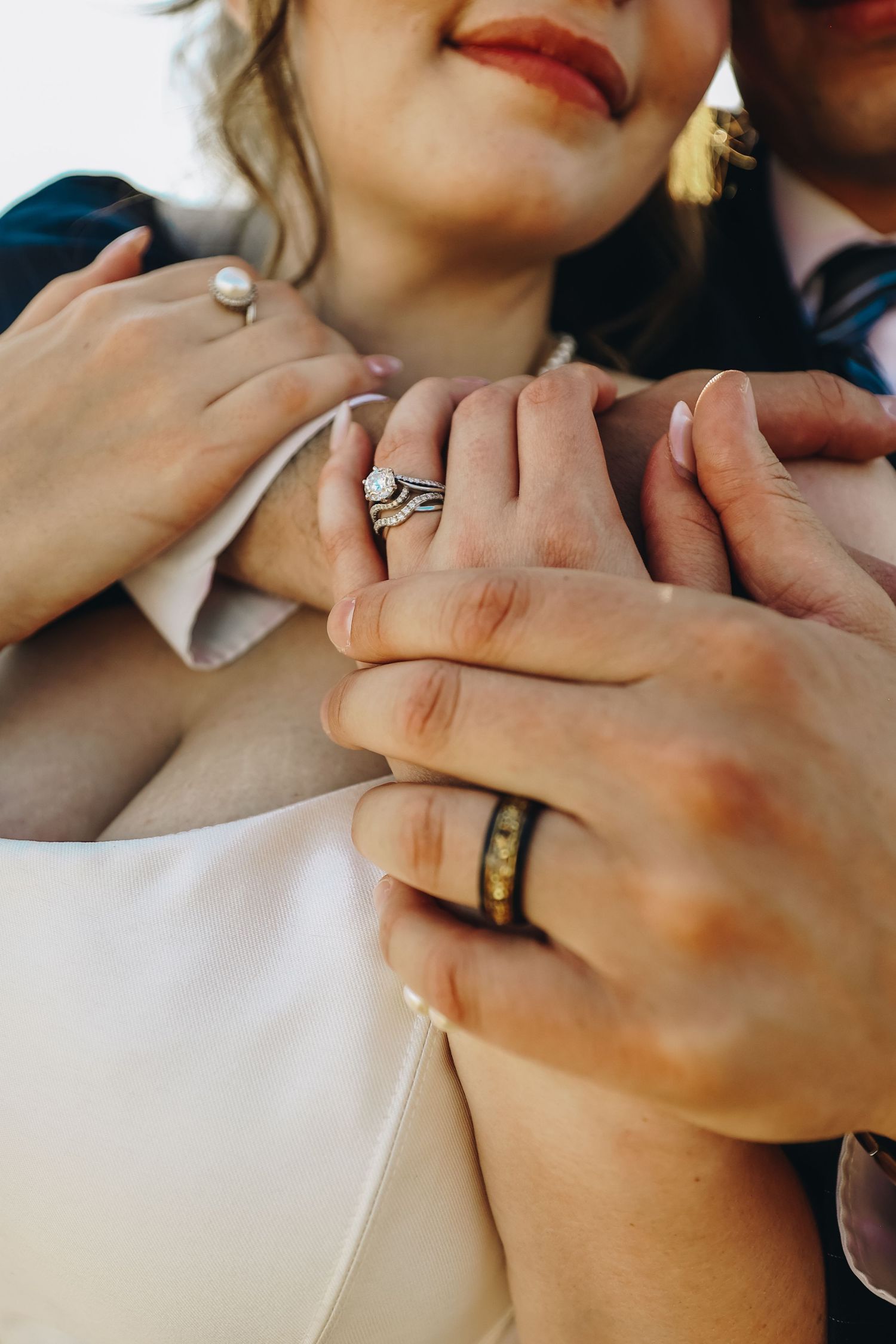 Close-up of bride and groom hands showing diamond wedding ring set and black tungsten band.