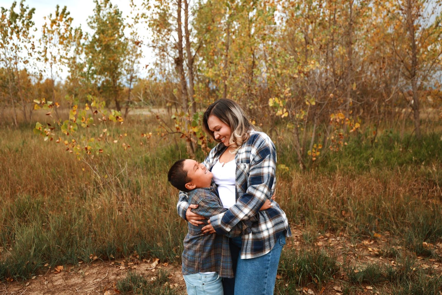 Mother and young son sharing a joyful embrace outdoors among colorful autumn trees and fall foliage.