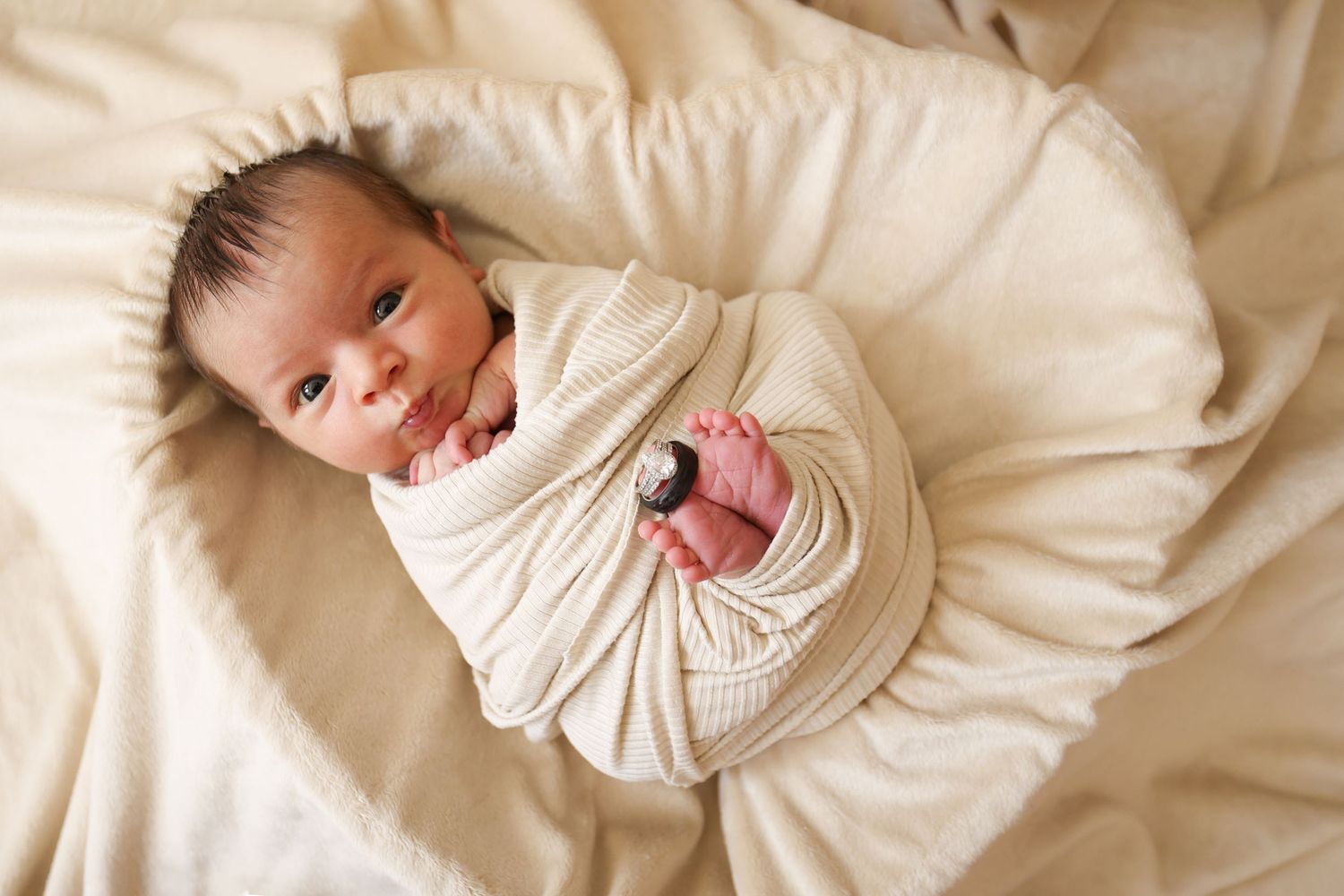 Alert newborn baby swaddled in cream wrap lying in soft bassinet, eyes open for lifestyle newborn photo.