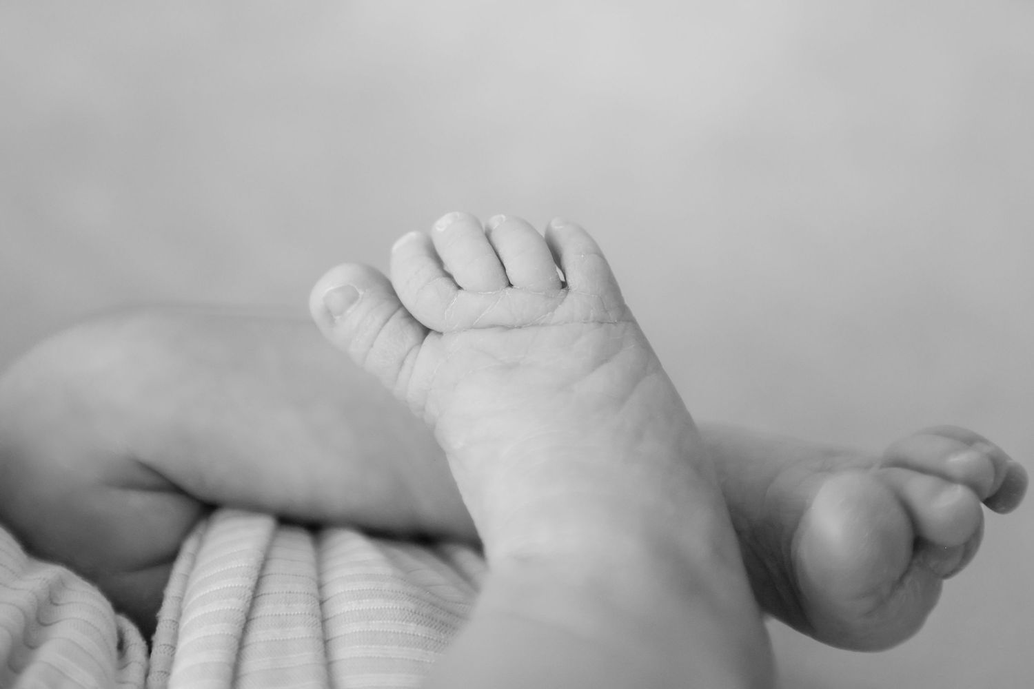 Close-up black and white photo of a newborn baby's tiny feet and toes resting on a soft blanket.