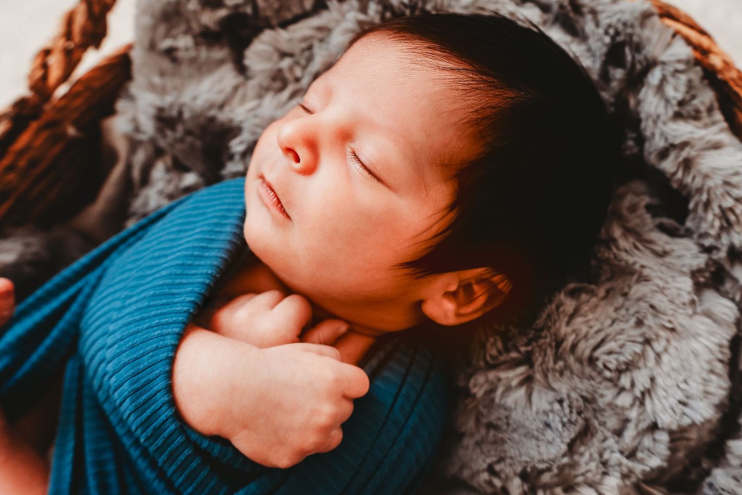 Peaceful newborn baby sleeping in basket wrapped in blue knit blanket.