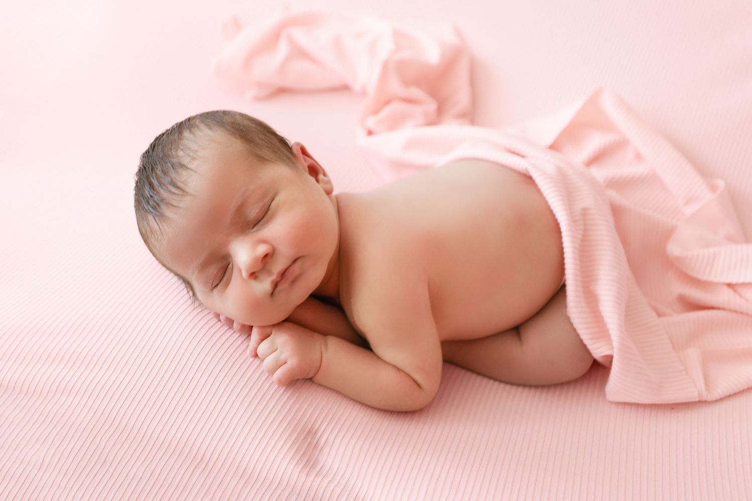 Peaceful newborn baby sleeping on pink blanket in classic curled pose for professional newborn photography.
