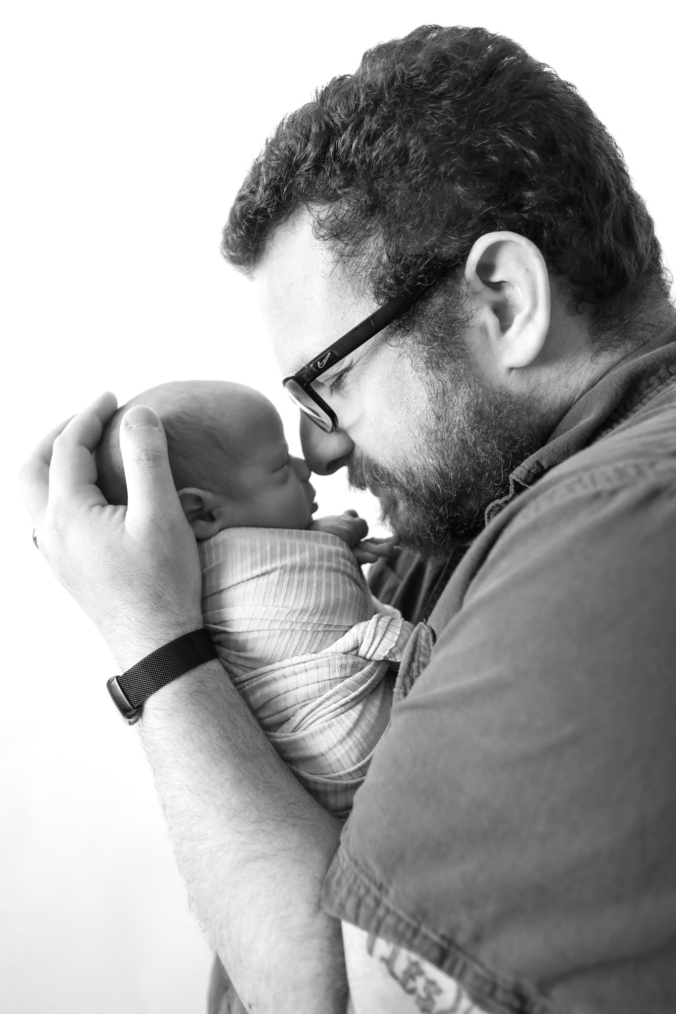 Black and white photo of a bearded father with glasses tenderly holding his newborn baby close to his face.