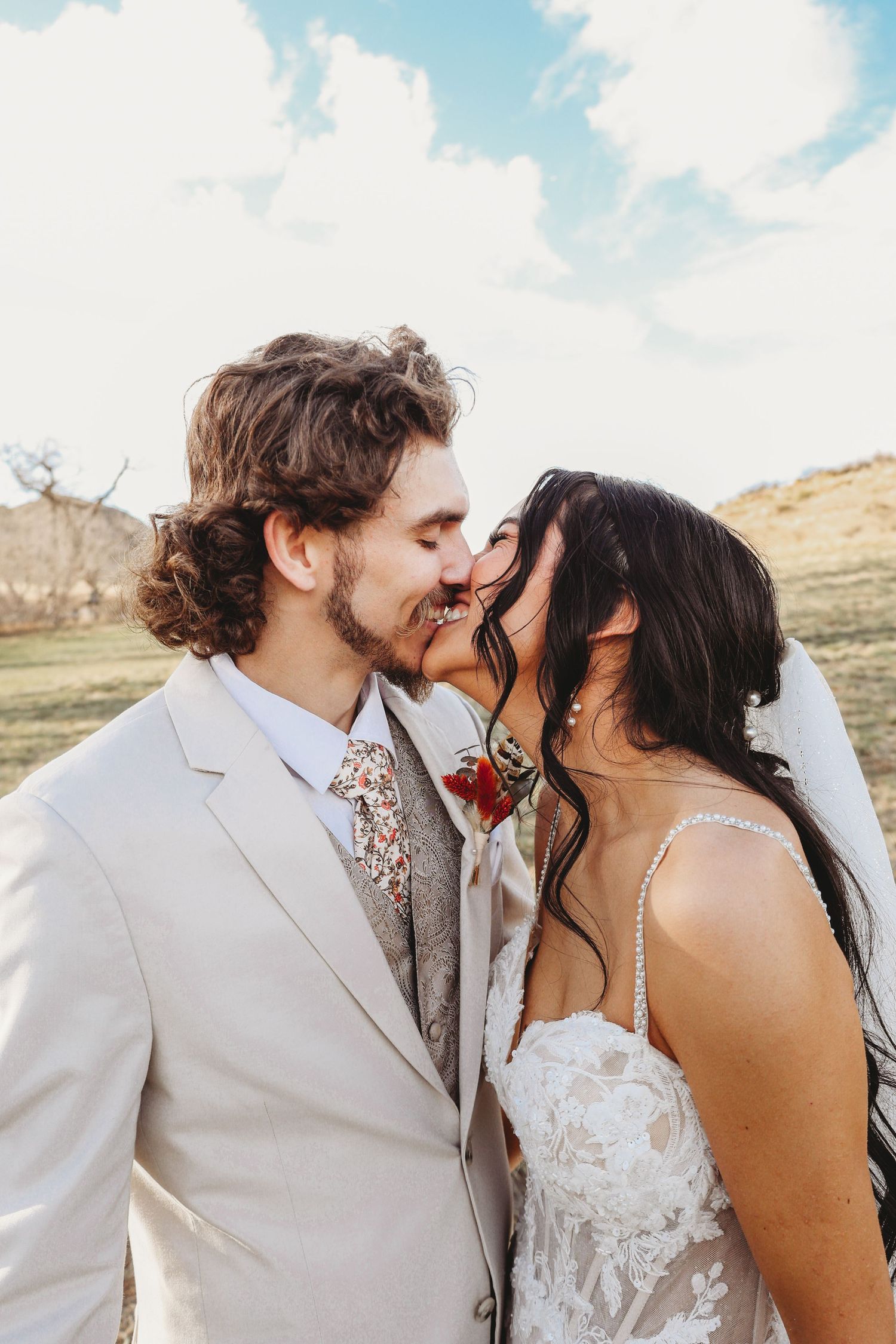 Bride and groom sharing romantic kiss outdoors with scenic countryside landscape in background.