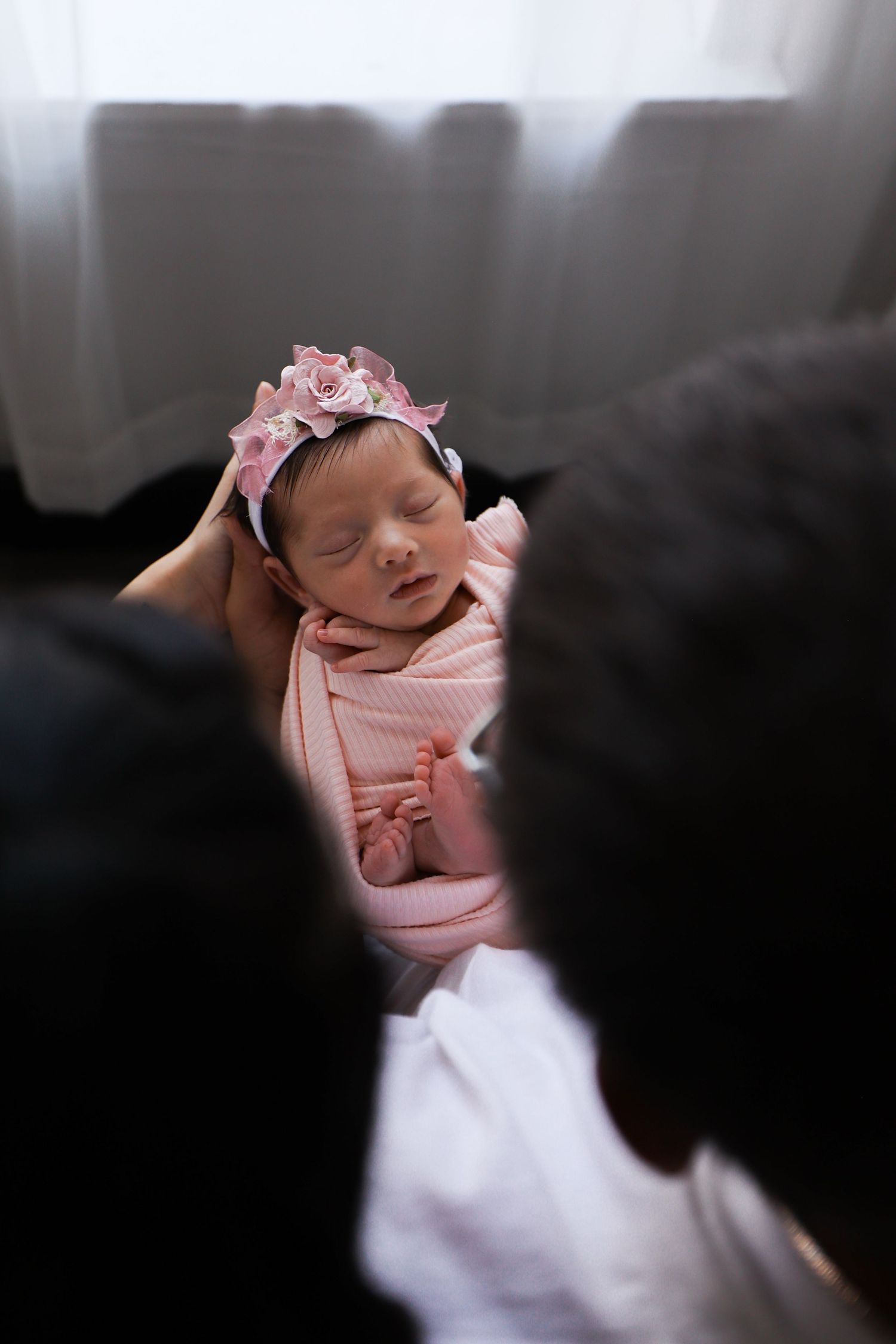 Parents lovingly gazing at their sleeping newborn baby girl swaddled in pink with a floral crown.