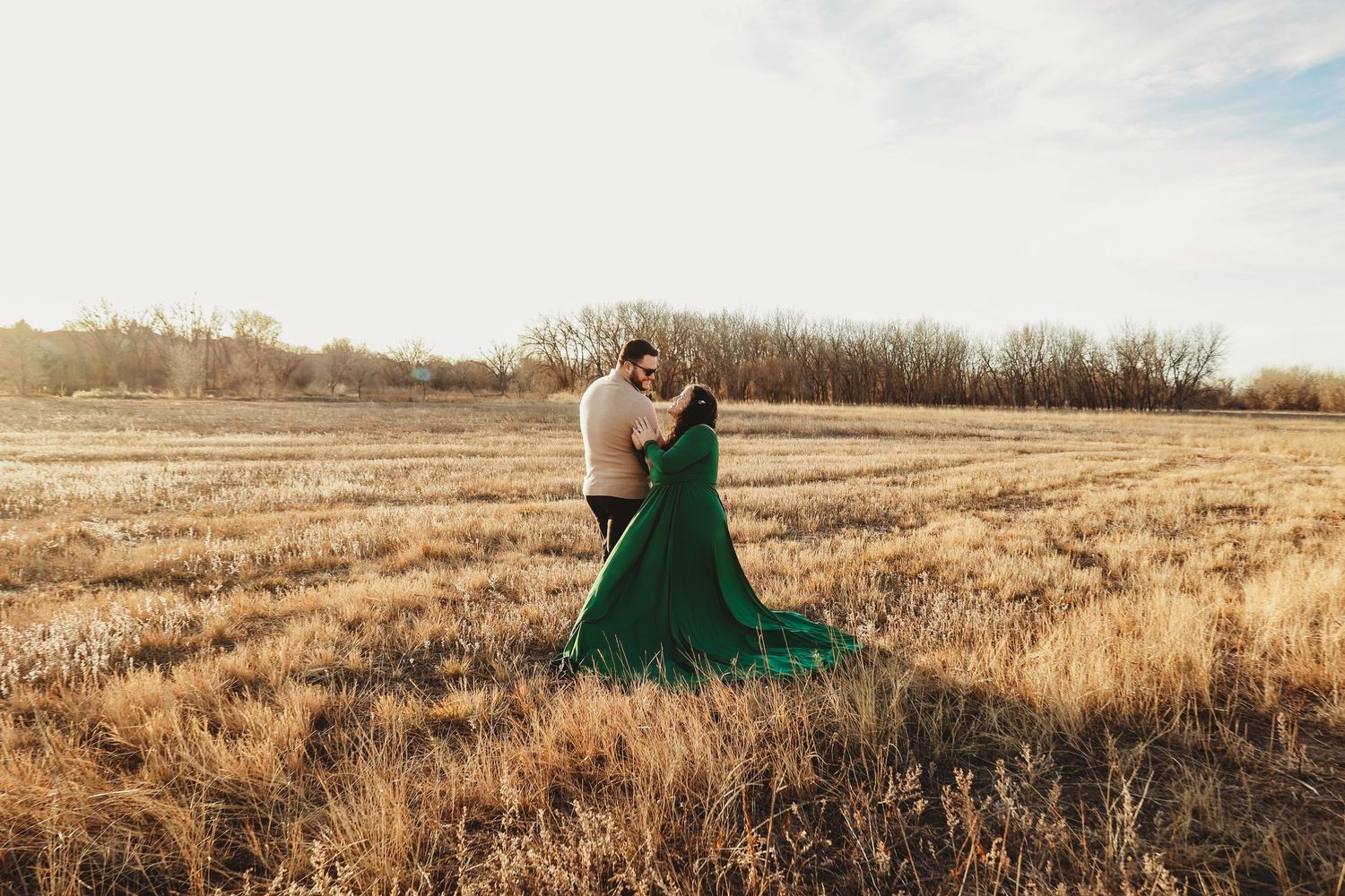Couple dancing in golden field at sunset, woman wearing flowing green gown.