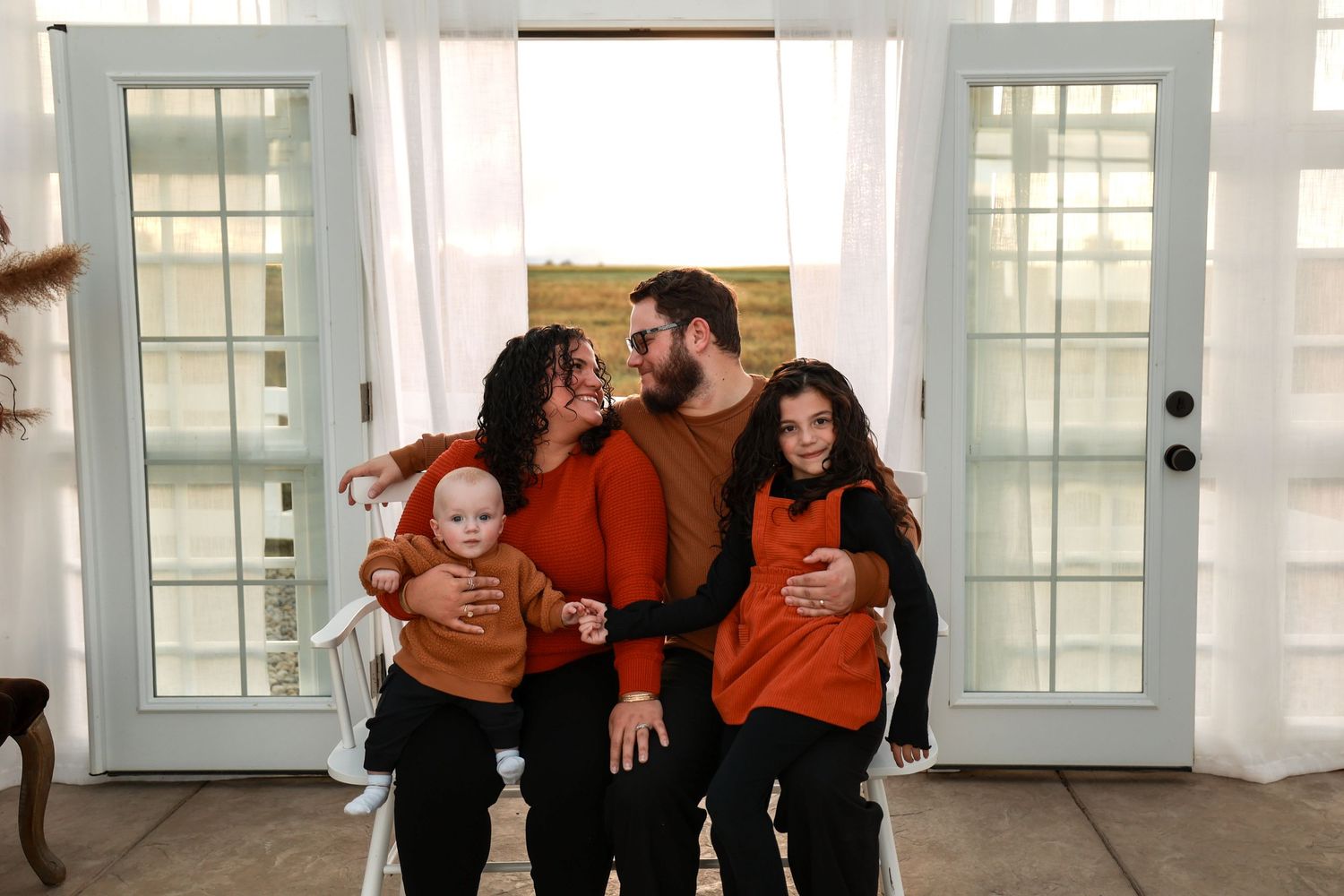 Family of four in matching rust orange outfits posing together near bright white French doors.