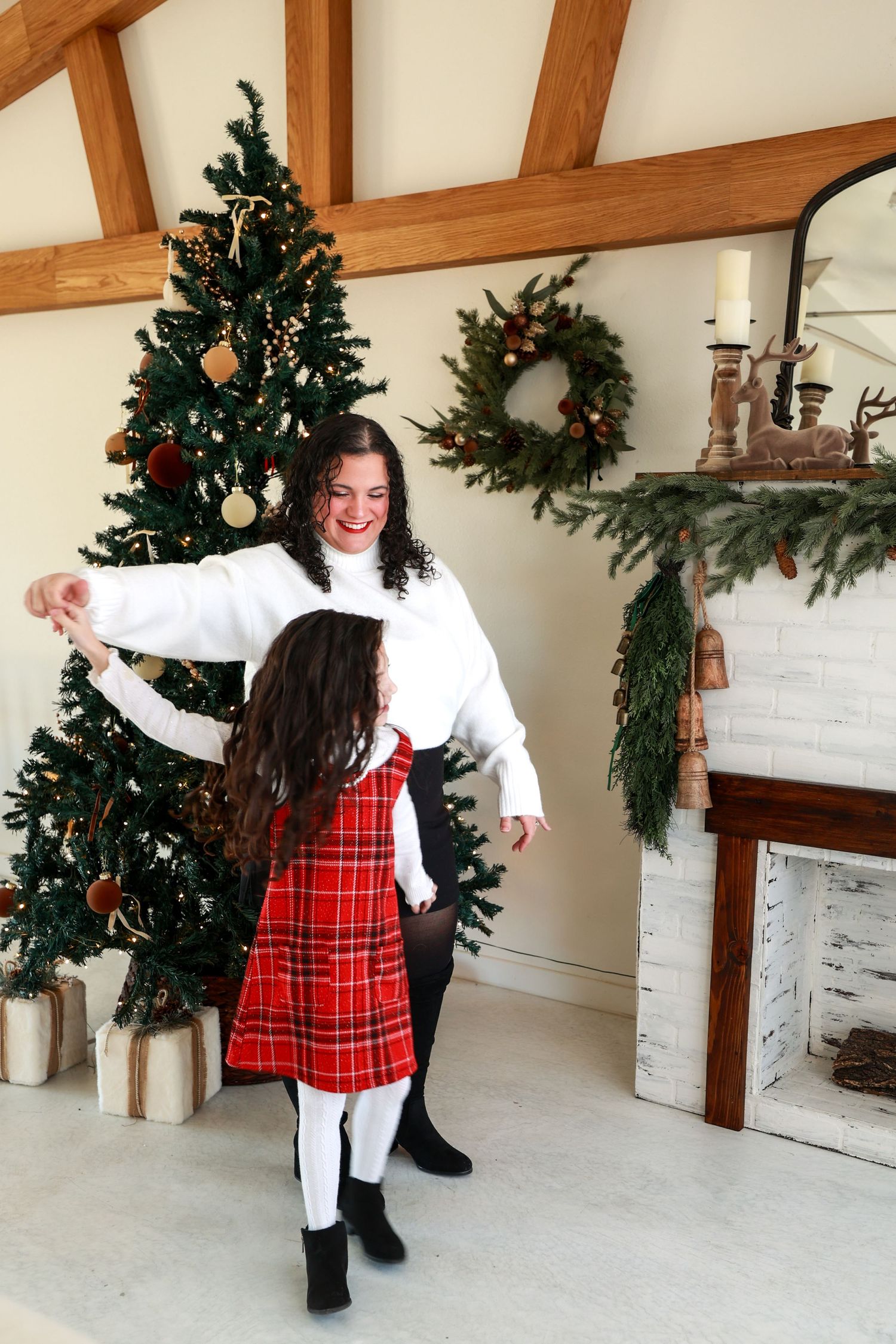 Mother and daughter dancing joyfully near decorated Christmas tree in festive living room.