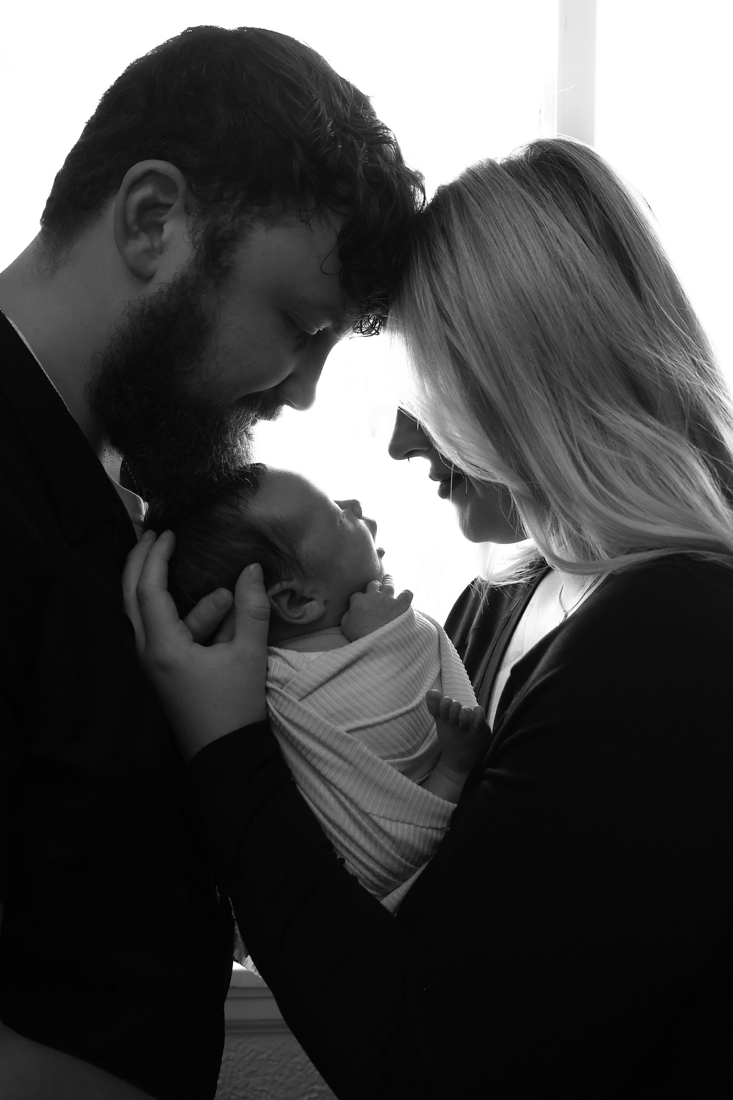Black and white photo of couple tenderly holding newborn baby together.