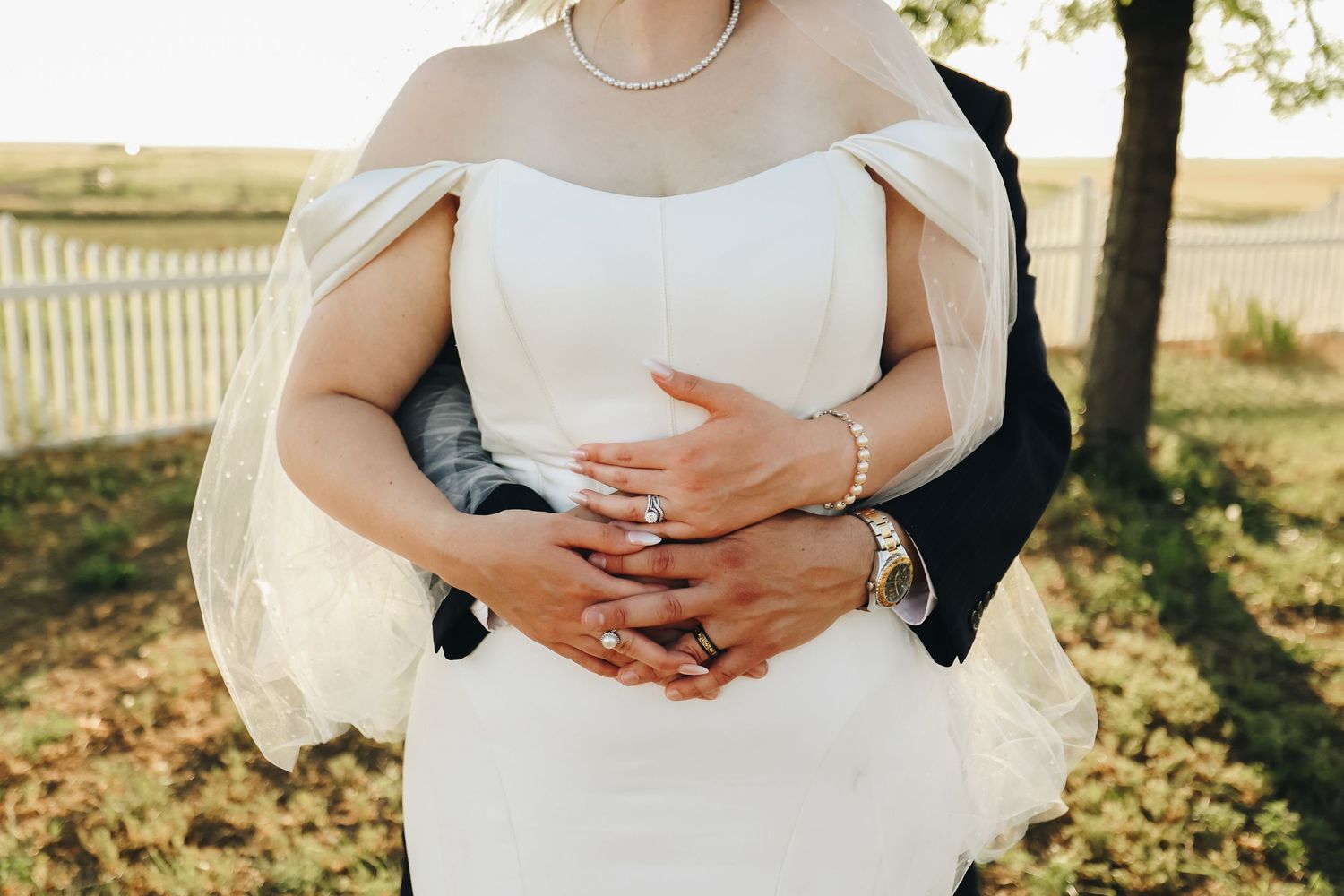 Close-up of bride and groom embracing, showcasing diamond ring, pearl bracelet, and off-shoulder gown.