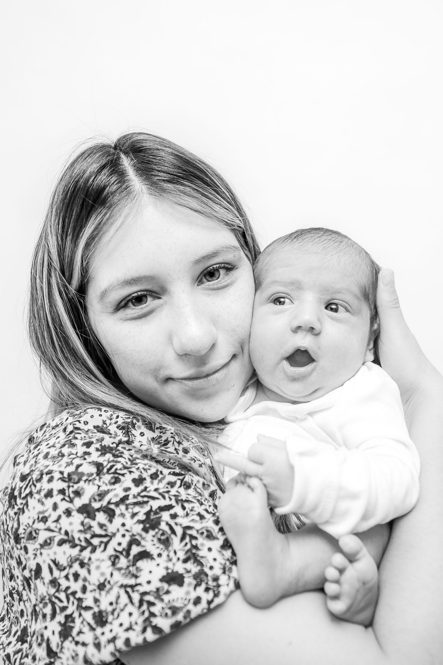 Black and white portrait of a young girl holding a newborn baby, both looking at the camera.