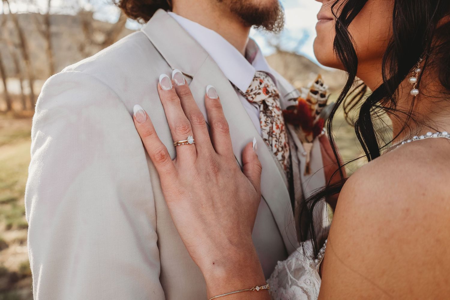 Close-up of bride placing her hand on grooms grey suit lapel, showing off her diamond engagement ring.