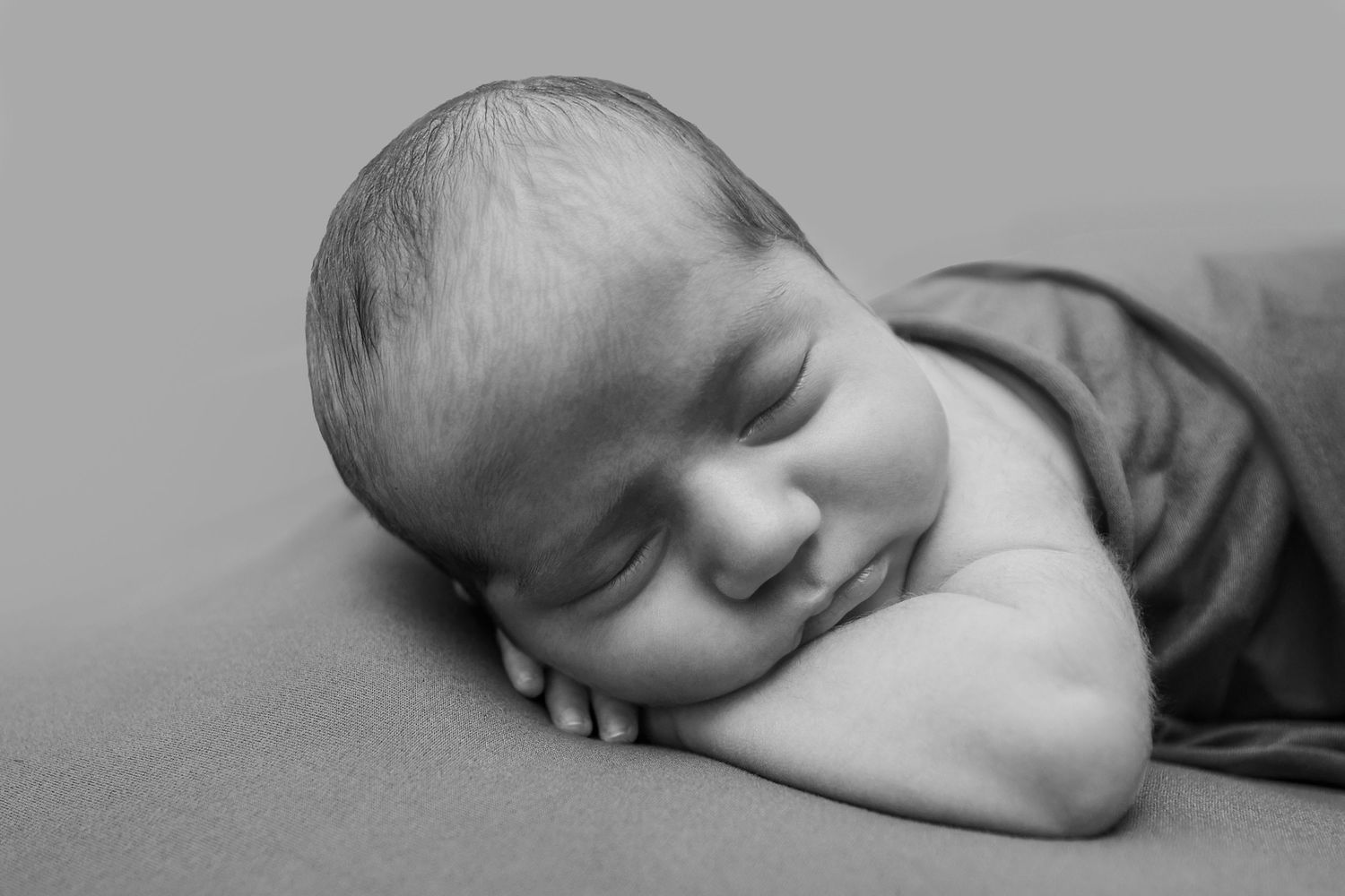 Black and white newborn photo of a sleeping baby smiling peacefully, wrapped in a soft blanket.