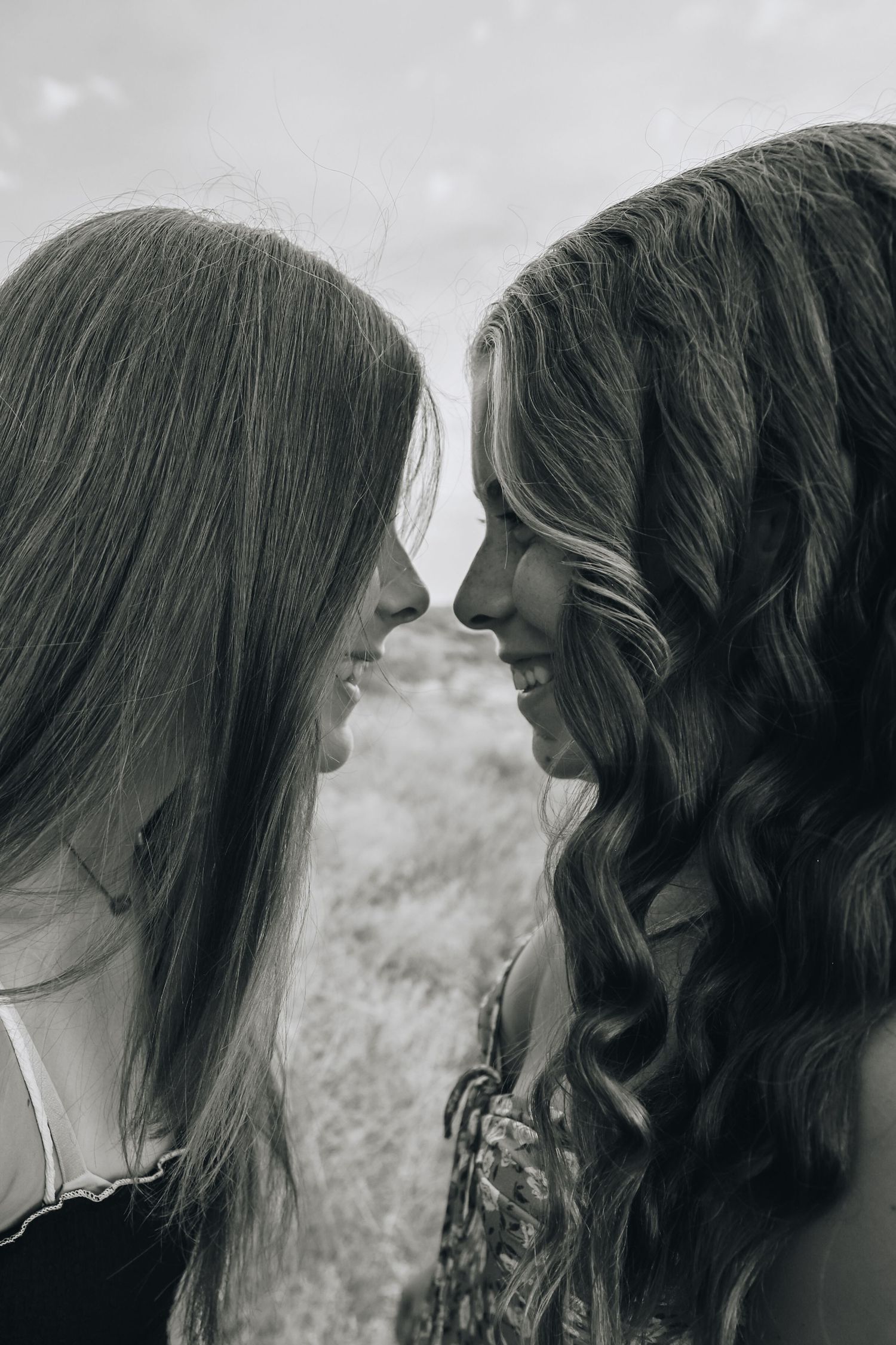 Black and white portrait of two young women facing each other closely in an outdoor field setting.