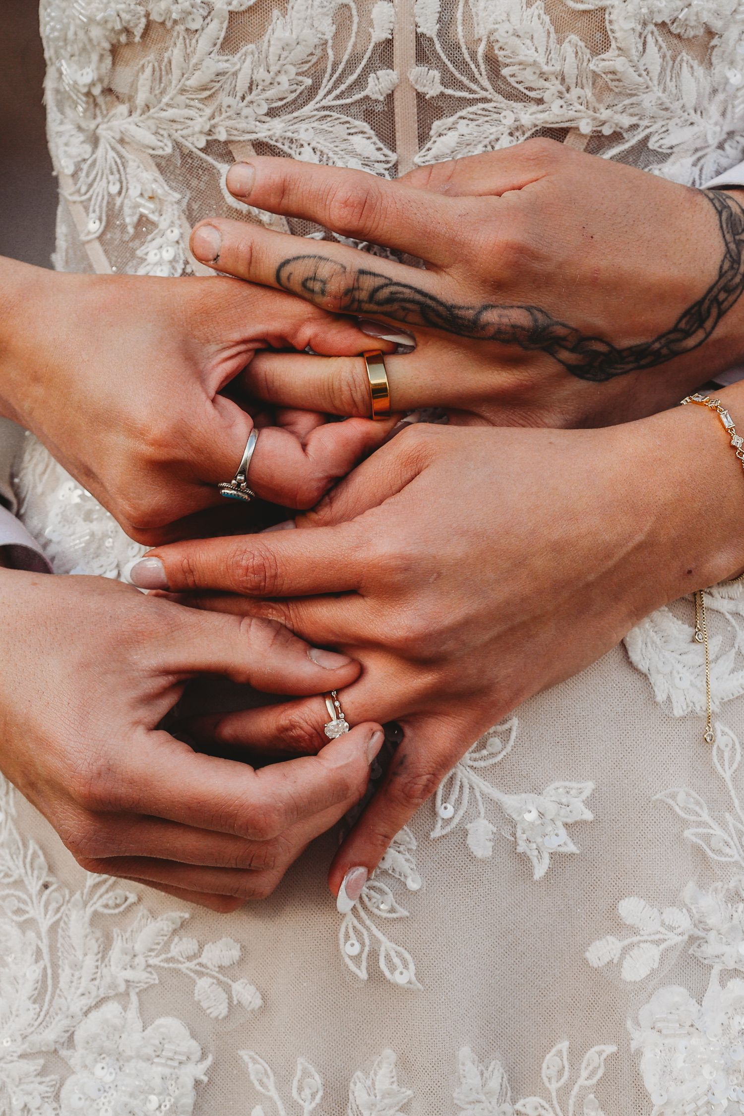 Close-up of bride and groom holding hands showing wedding rings, with tattoos visible on the grooms arm.