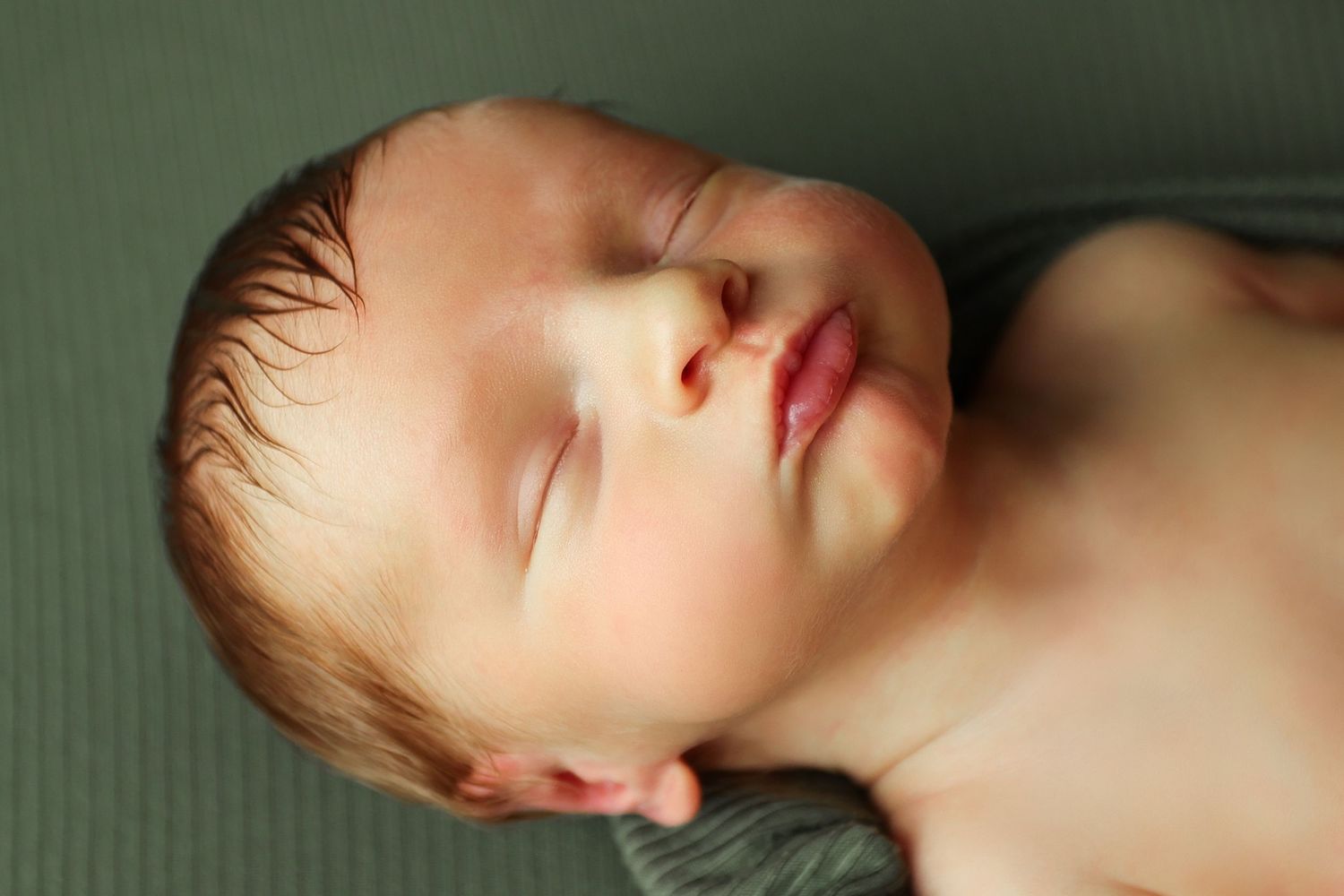 Close-up portrait of a peacefully sleeping newborn baby on a soft green background.