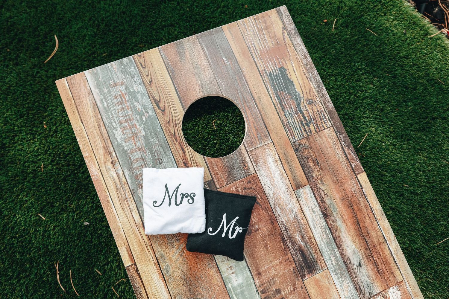 Rustic wooden cornhole board with Mr and Mrs bean bags on green grass at a wedding outdoor game setup.