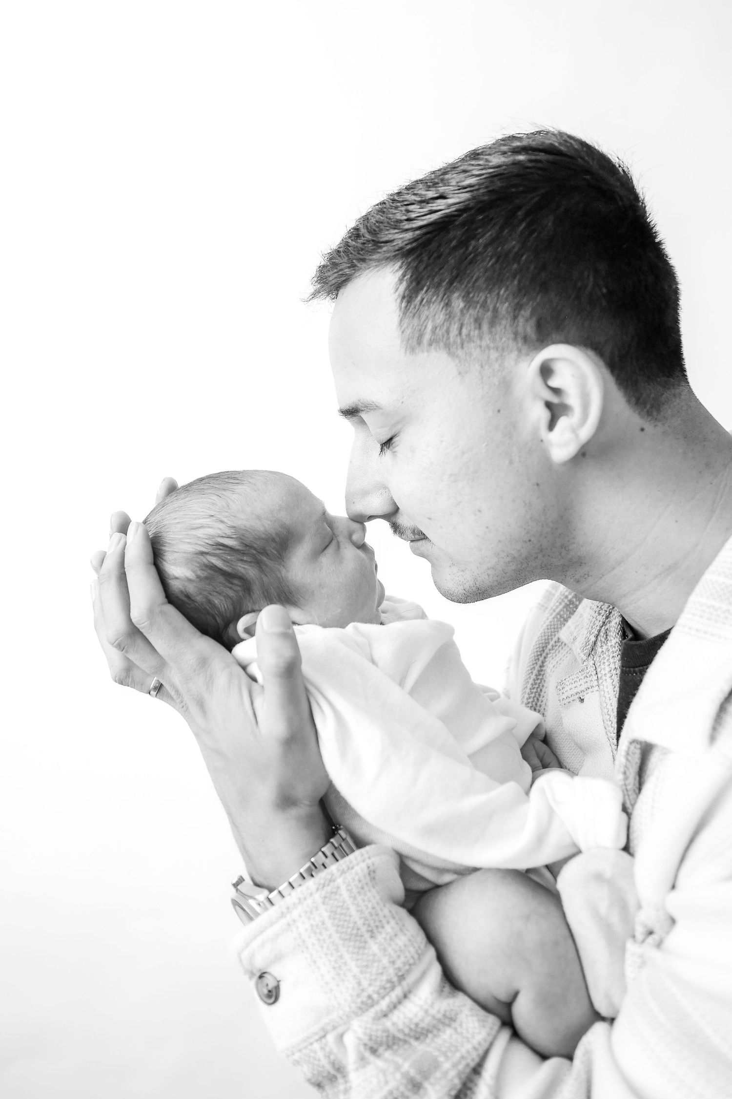 Black and white photo of a father tenderly holding his newborn baby face-to-face in an intimate bonding moment.
