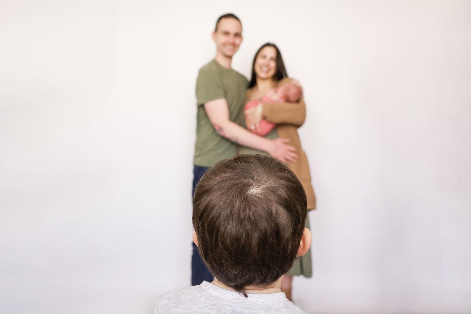 Parents holding newborn baby smiling while older child stands in foreground.