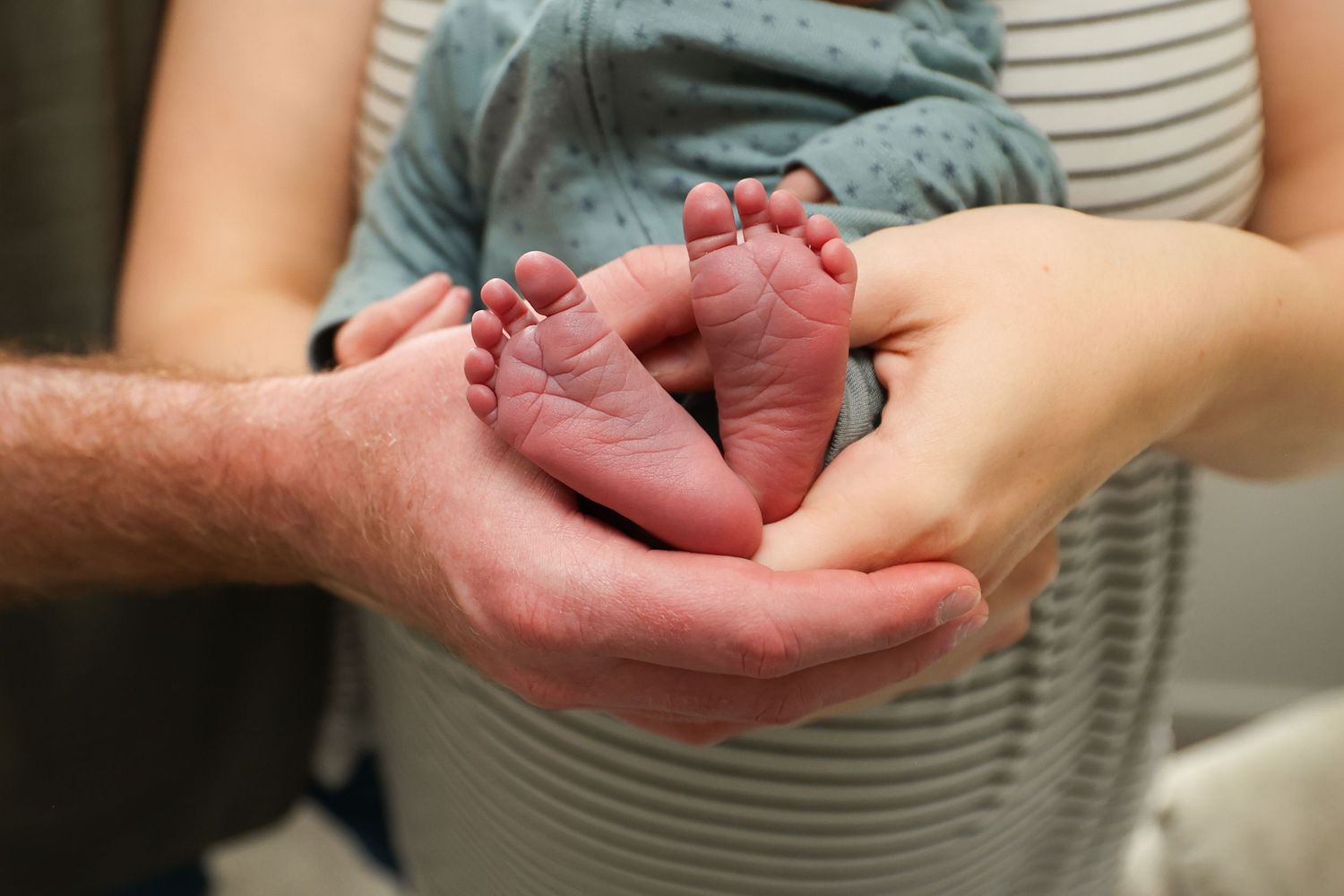 Parents cradling tiny newborn baby feet in their hands close-up.