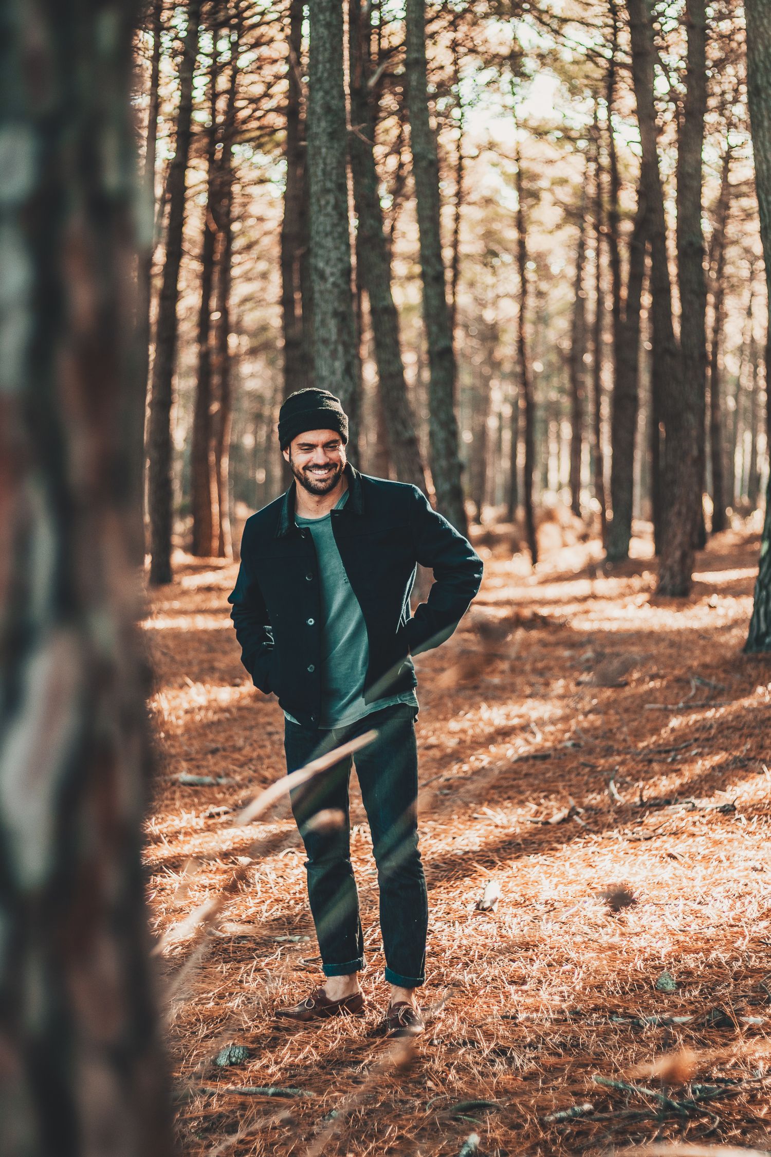 Personne en vêtements d'hiver posant parmi de grands pins dans une forêt d'automne.