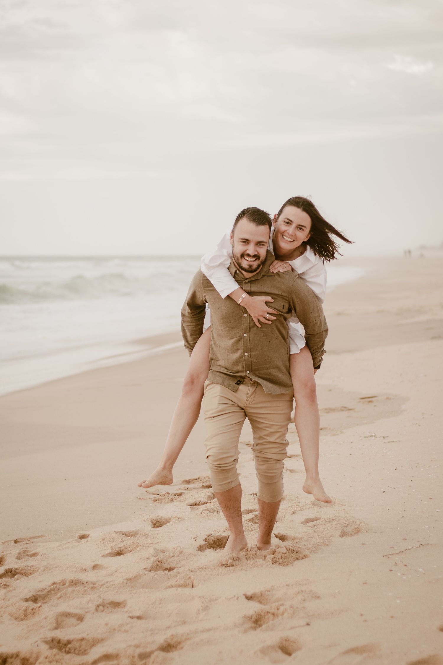 Un moment ludique de tour d'un couple capturé sur une plage de sable avec un ciel couvert en arrière-plan.