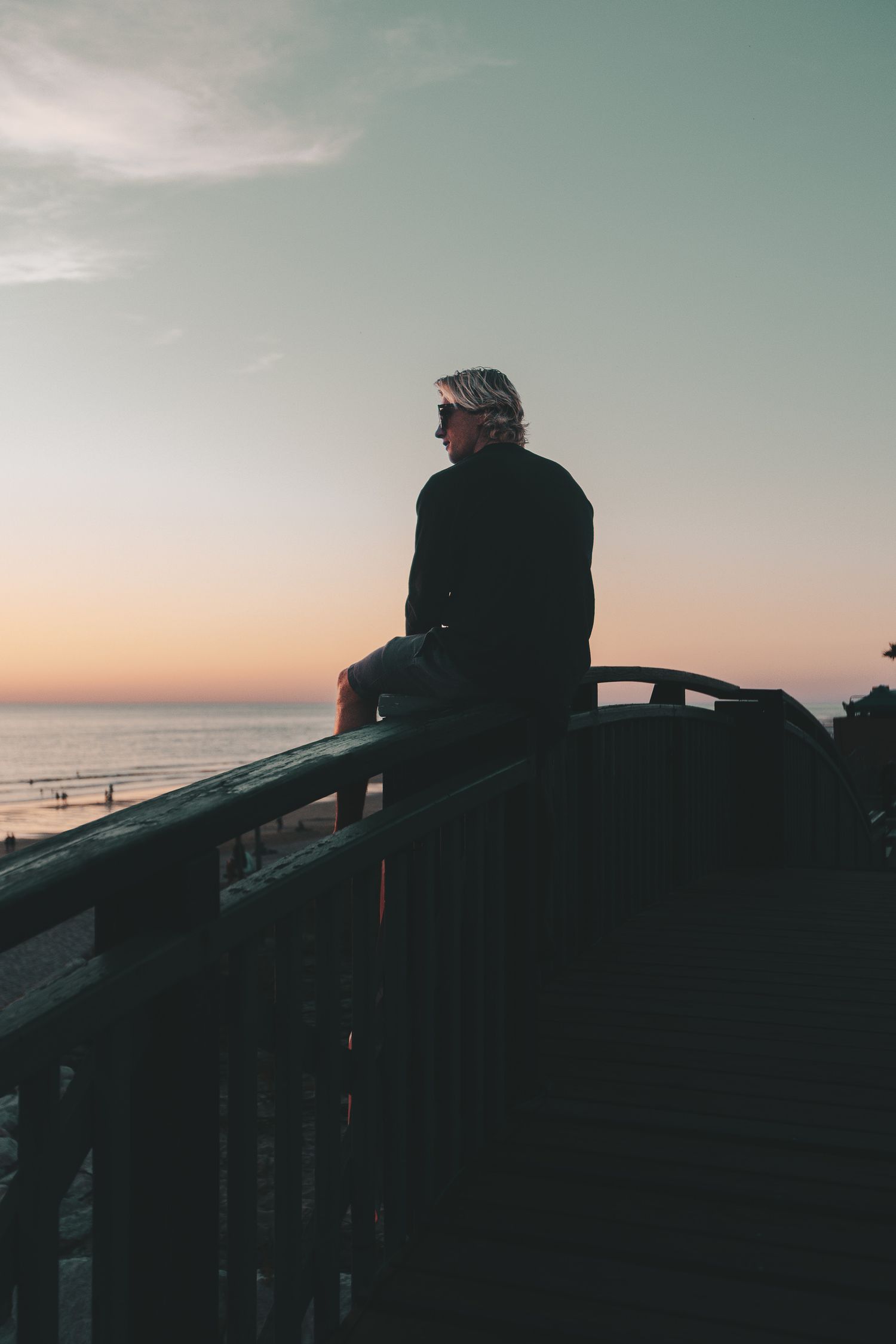 Personne assise sur une balustrade en bois donnant sur la plage pendant le coucher du soleil.