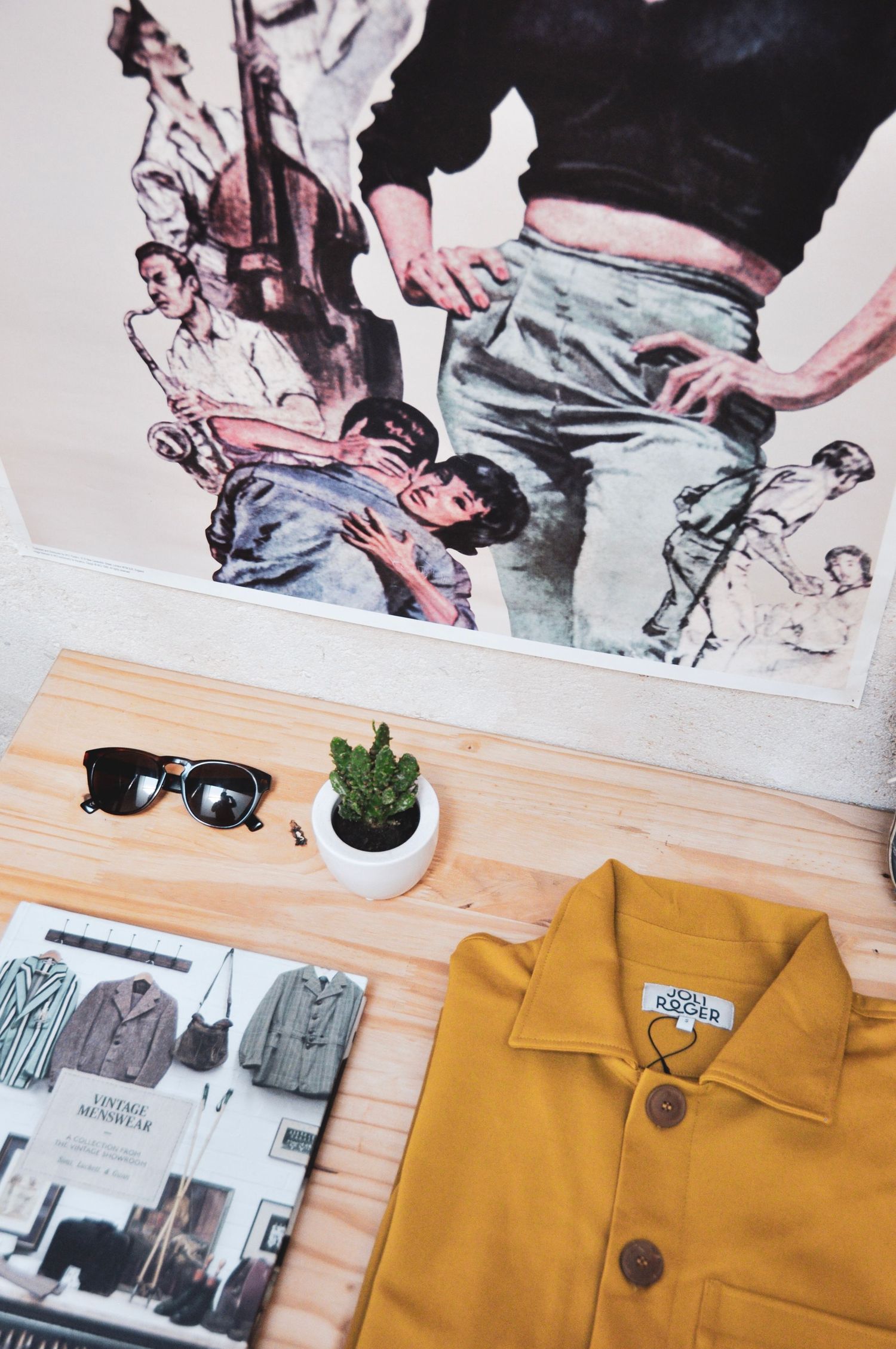 Flatlay d'une veste jaune, de lunettes de soleil, d'une petite plante en pot et d'un magazine de mode sur une surface en bois avec des œuvre