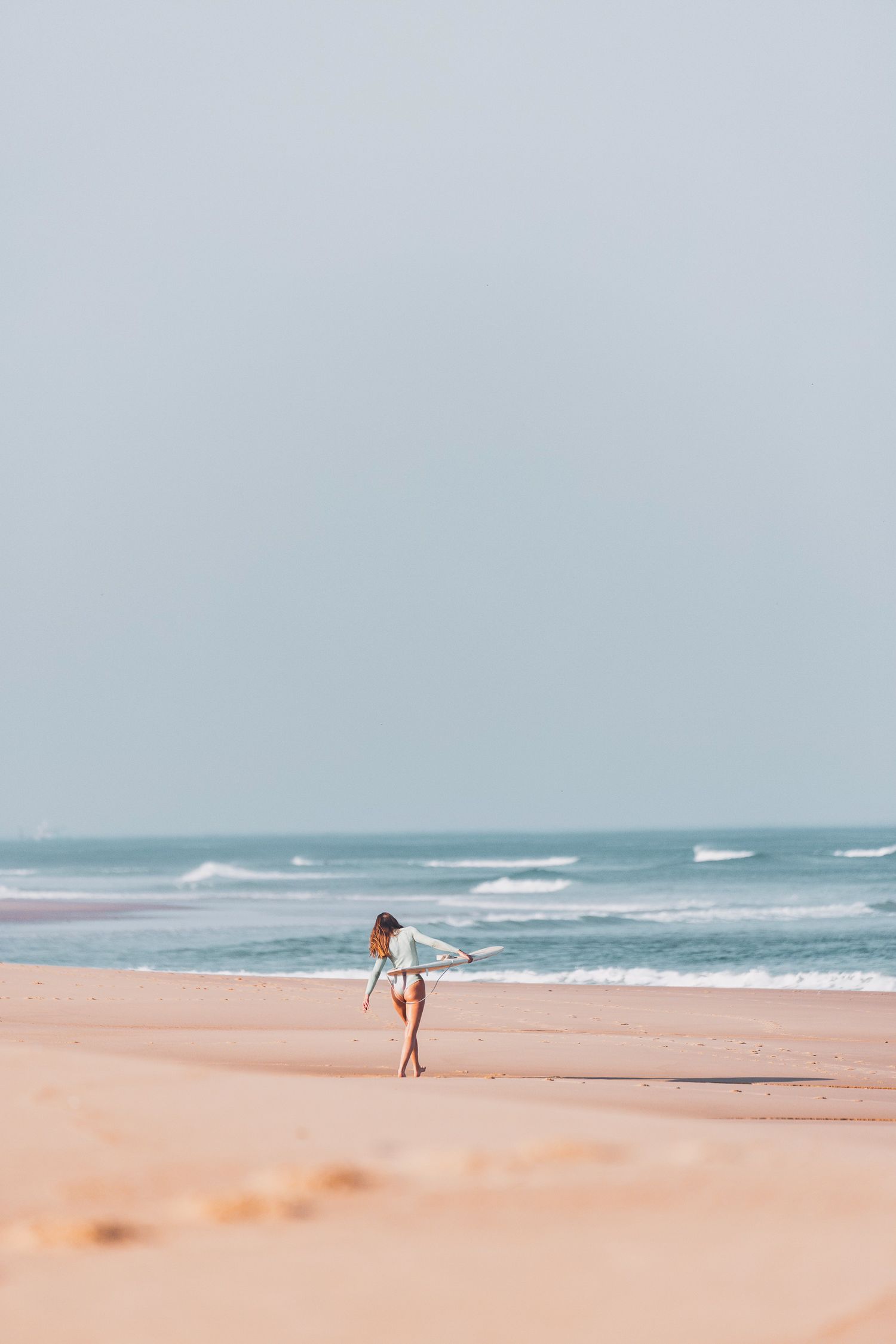 Une personne marche le long d'une plage sereine avec des vagues qui s'écrasent et du sable rose doux sous un ciel bleu .
