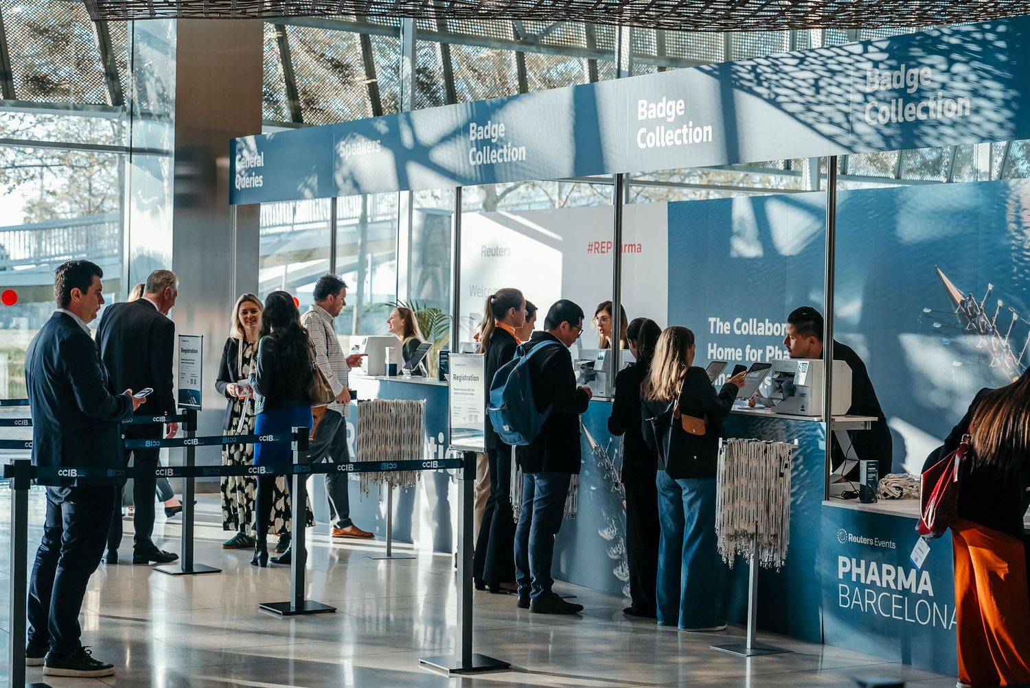 People wait in line at a modern event check in desk with blue-tinted glass walls.