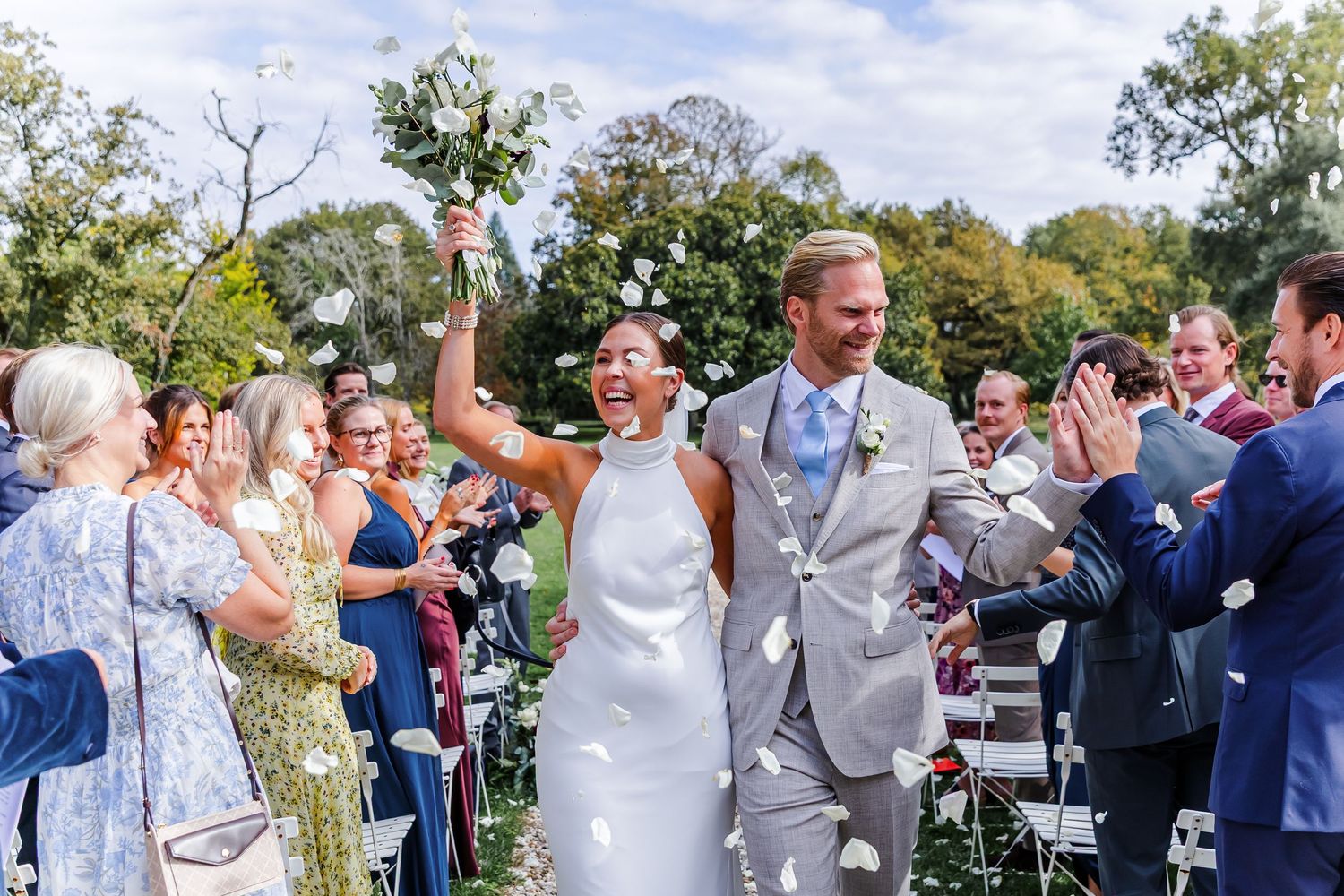 Wedding guests celebrate with confetti and cheers during an outdoor ceremony on a sunny autumn day.