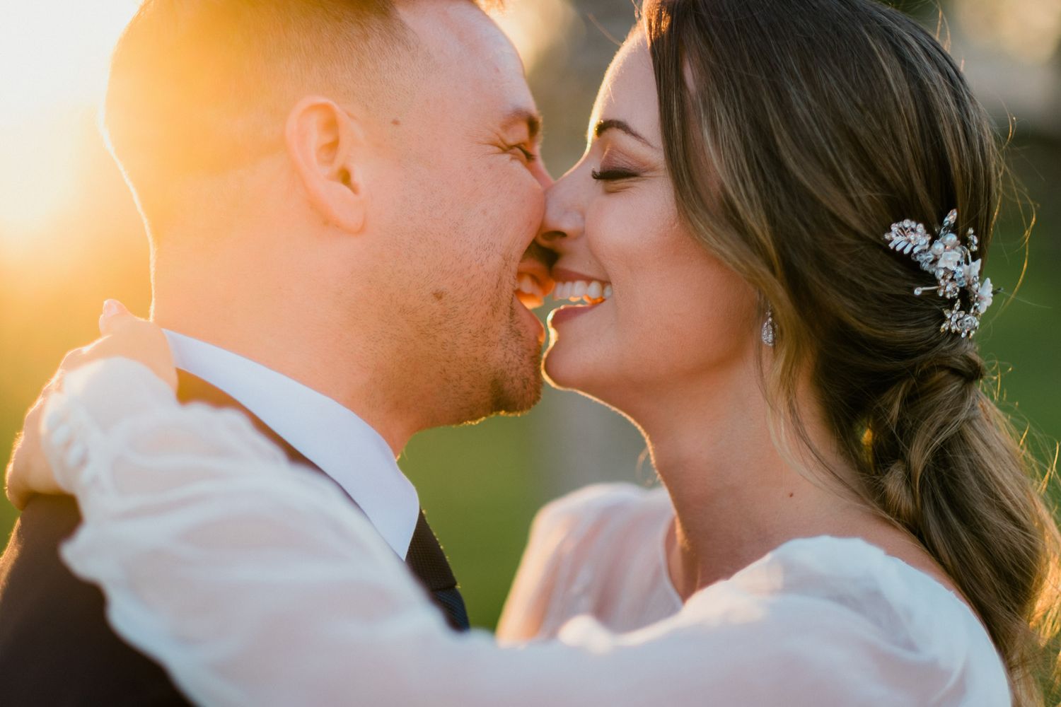 Romantic couple shares tender kisses in golden sunlight during outdoor wedding photo session.