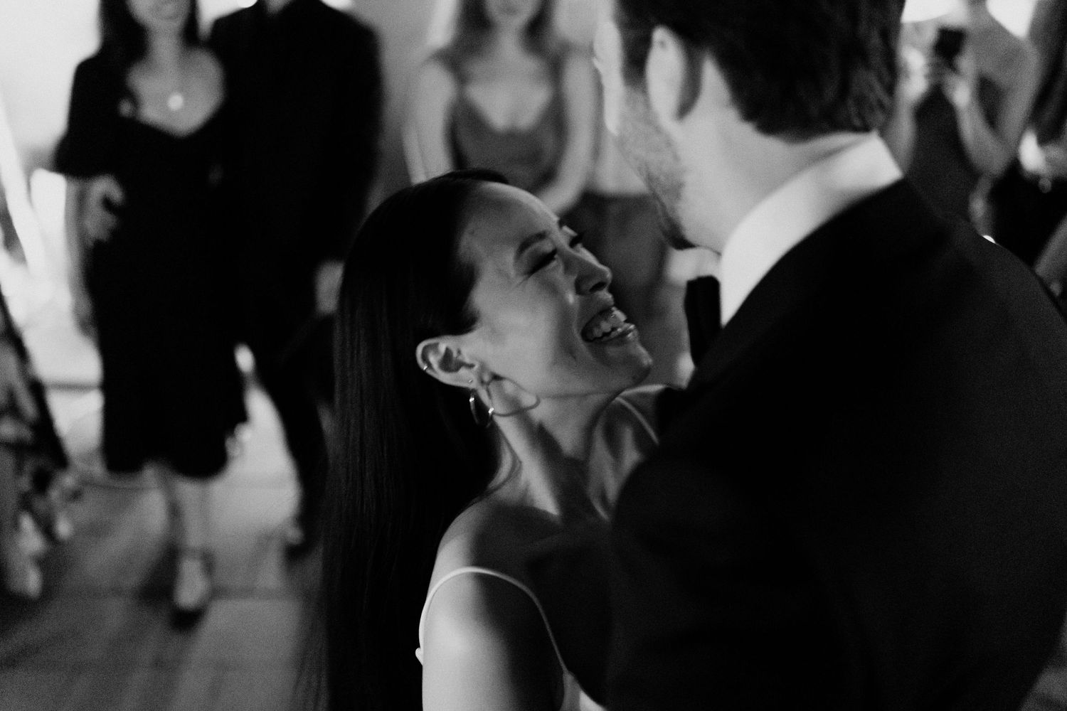 A black and white photo of a bride and groom dancing with guests at their wedding reception.