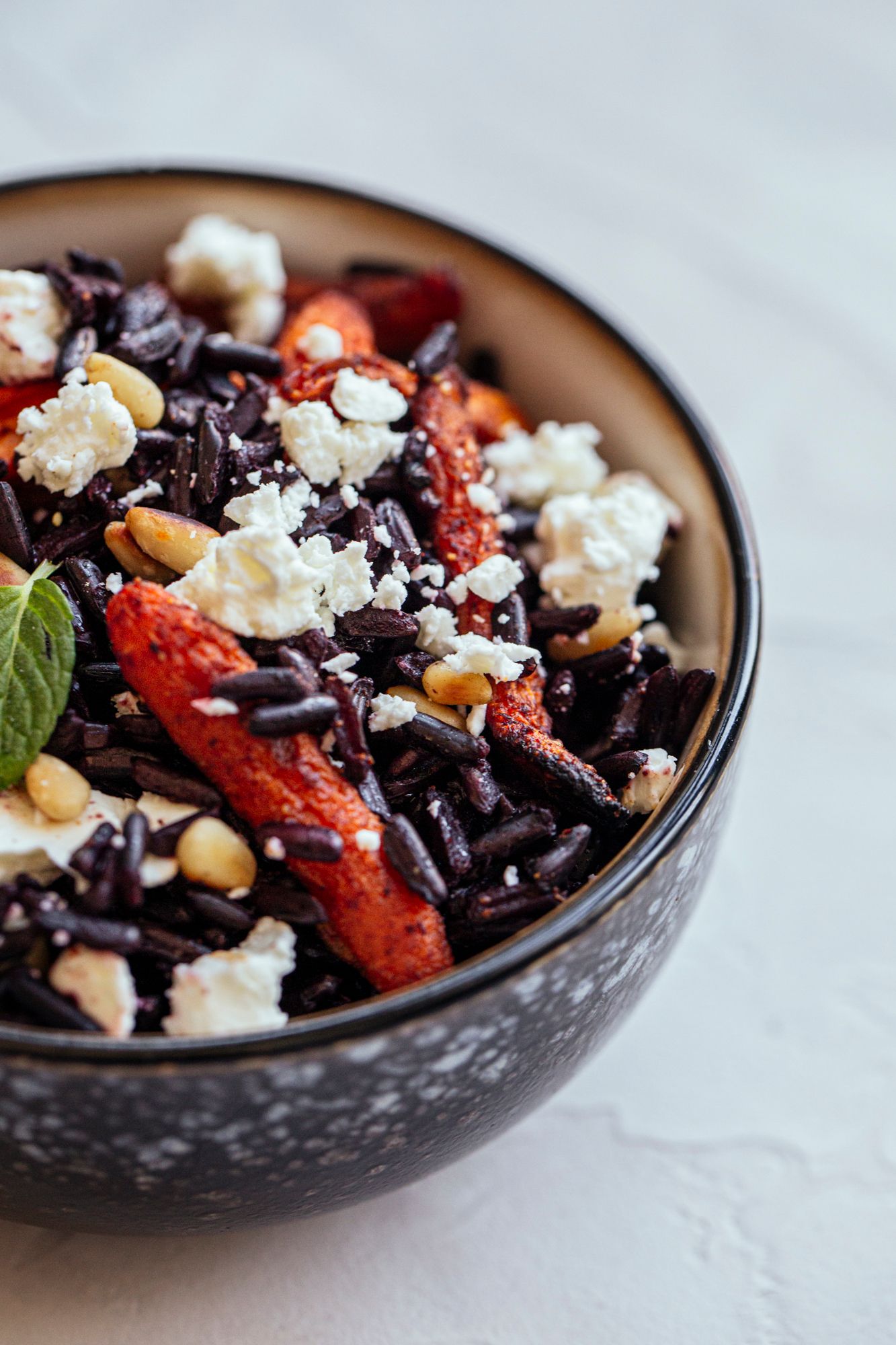 Vibrant black rice bowl with crumbled feta, roasted red peppers and fresh herbs.