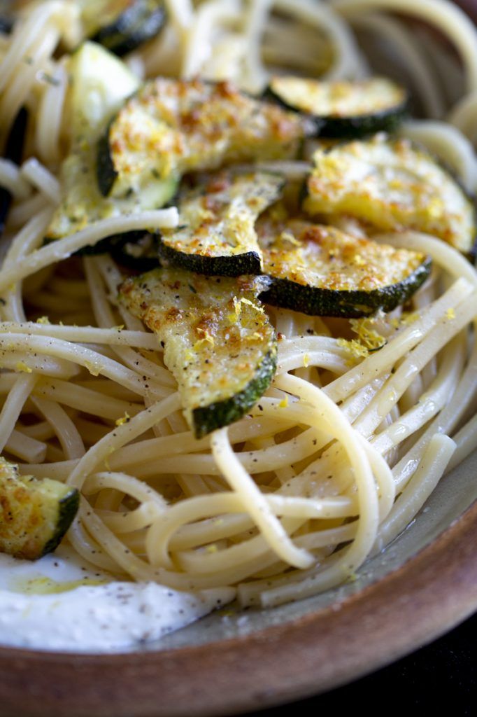 Close-up of spaghetti with roasted zucchini slices and herbs in a terracotta dish.