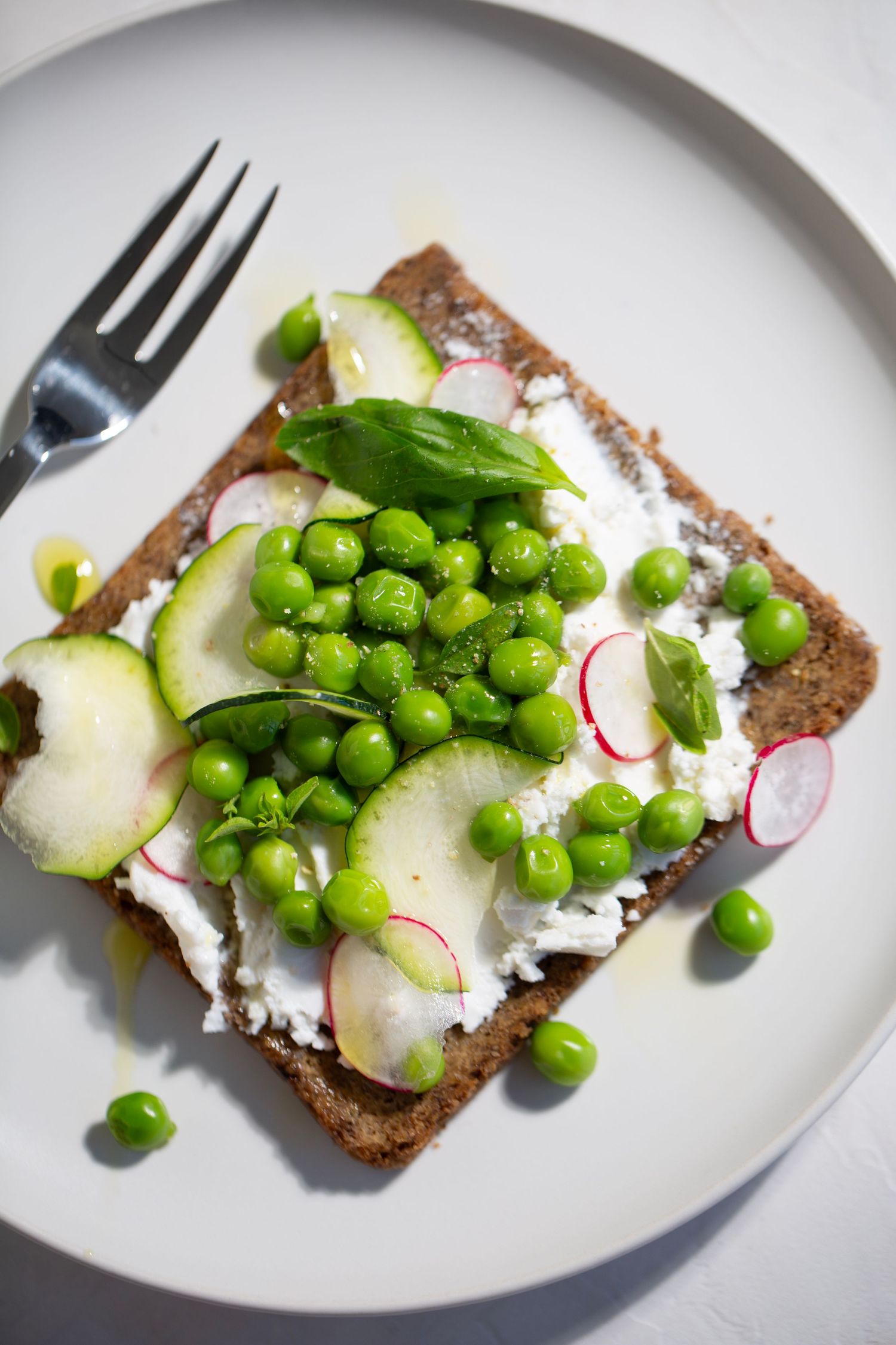 Open-faced sandwich with cream cheese, radishes, cucumber slices and fresh green peas on dark bread.