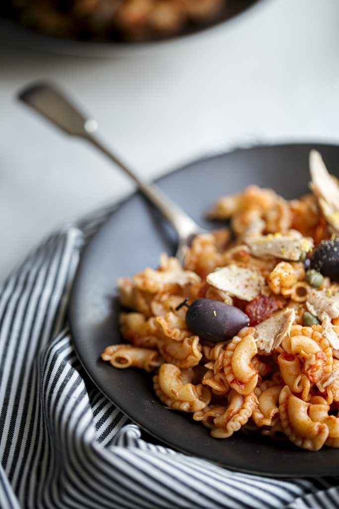 Pasta salad with olives and garnish served on a black plate with striped napkin.