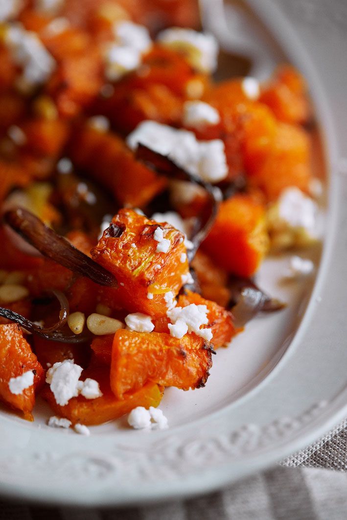 Roasted butternut squash cubes topped with crumbled feta cheese and fresh herbs on an elegant white plate.