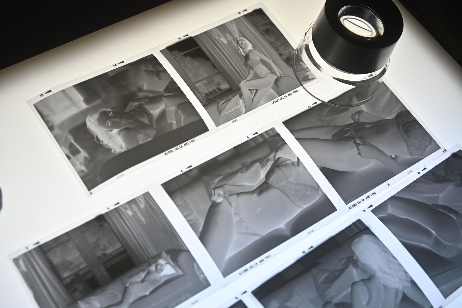 Black and white film negatives laid out on a white surface with a camera lens visible in the corner.