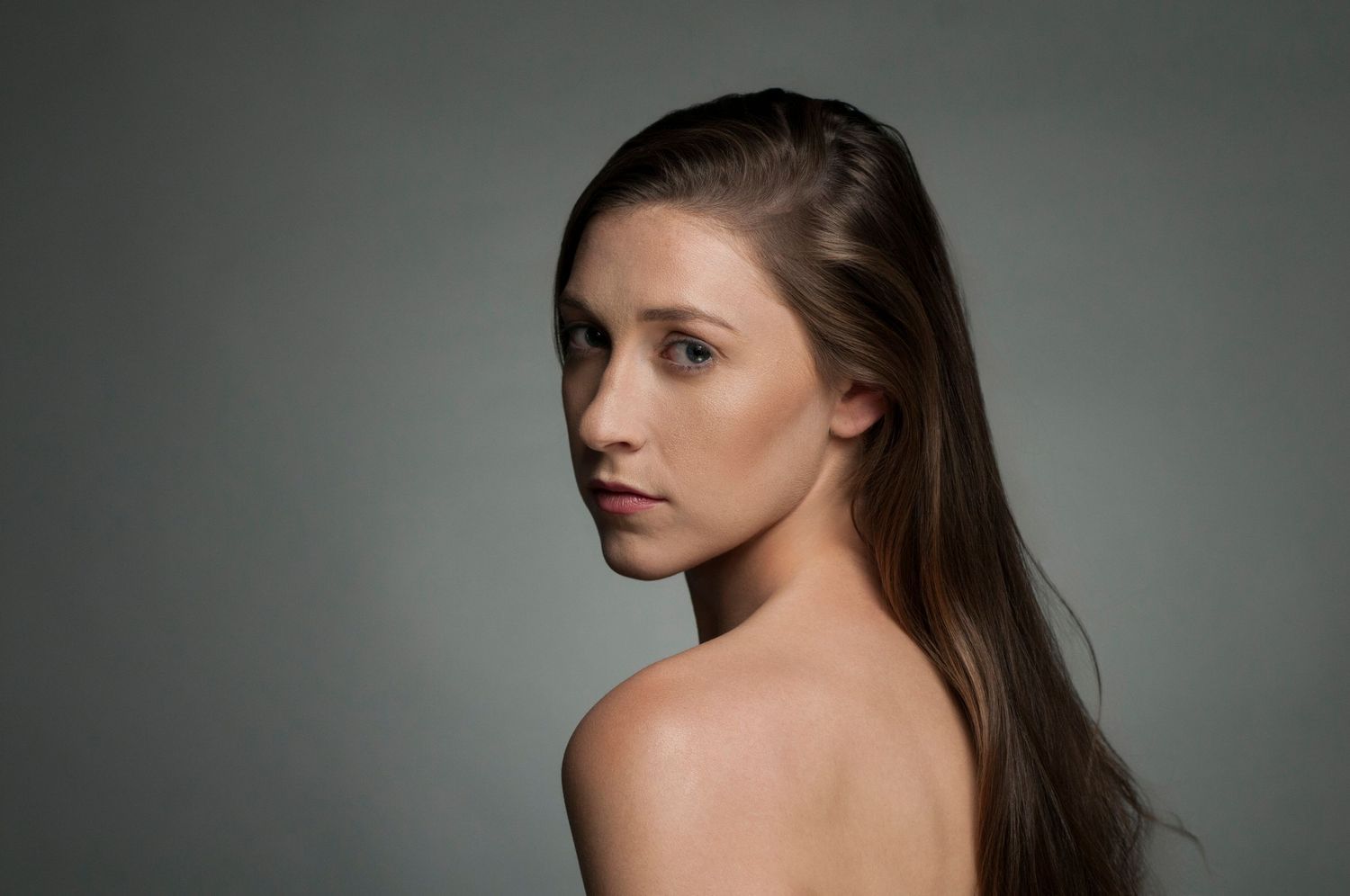 Elegant profile portrait showing bare shoulders and long dark hair against neutral background.