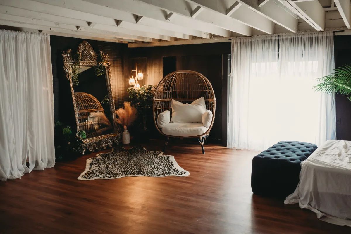 Cozy bohemian reading nook with hanging egg chair, dark wall mural, and hardwood floors in natural lighting.