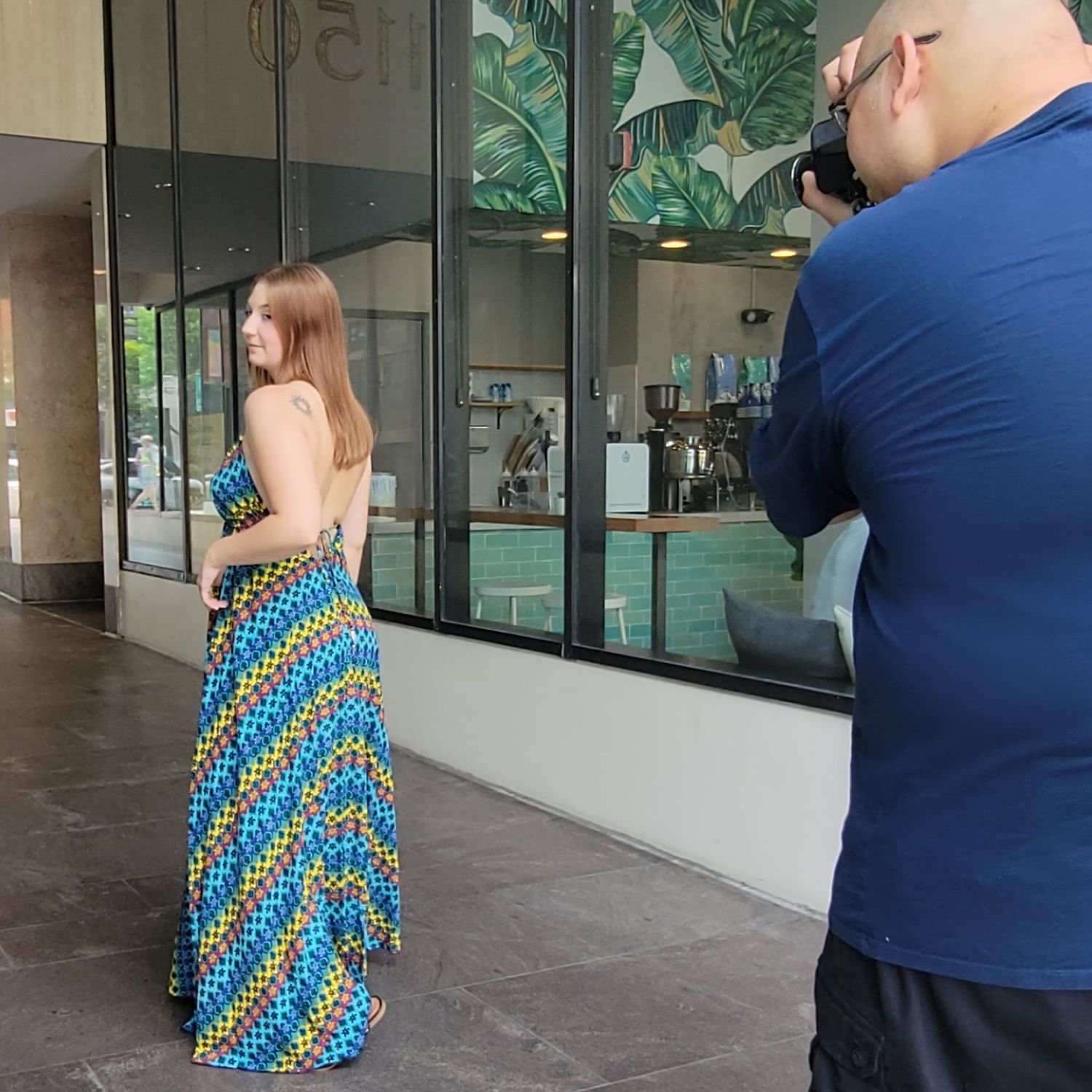 A photo shoot in progress outdoors with a photographer capturing someone wearing a vibrant blue and yellow patterned maxi dress.
