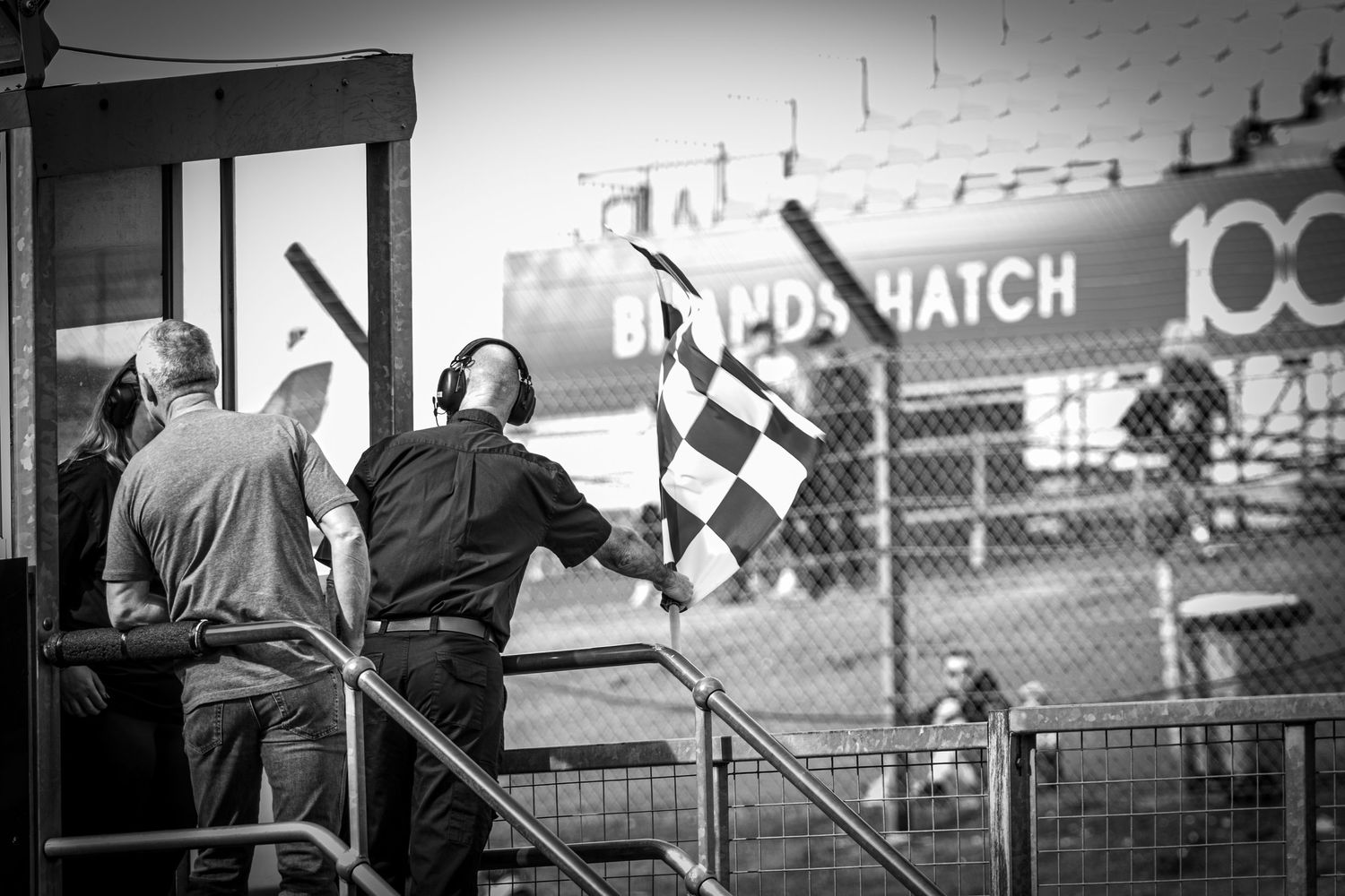Black and white image of a marshal waving a checkered flag at Brands Hatch racing circuit.