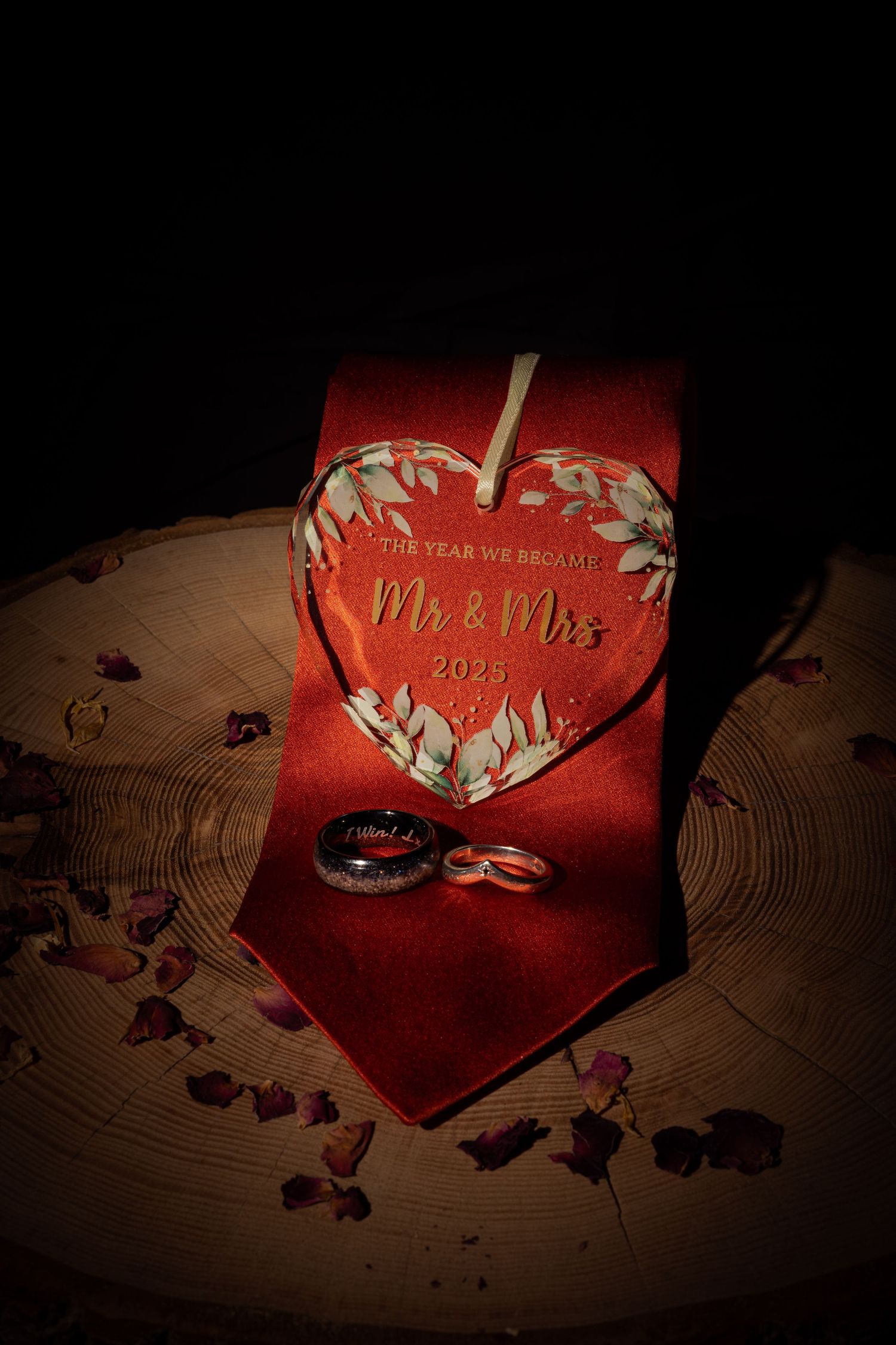 Wedding rings resting on a orange tie beside a heart-shaped Mr and Mrs 2025 keepsake ornament and wedding rings