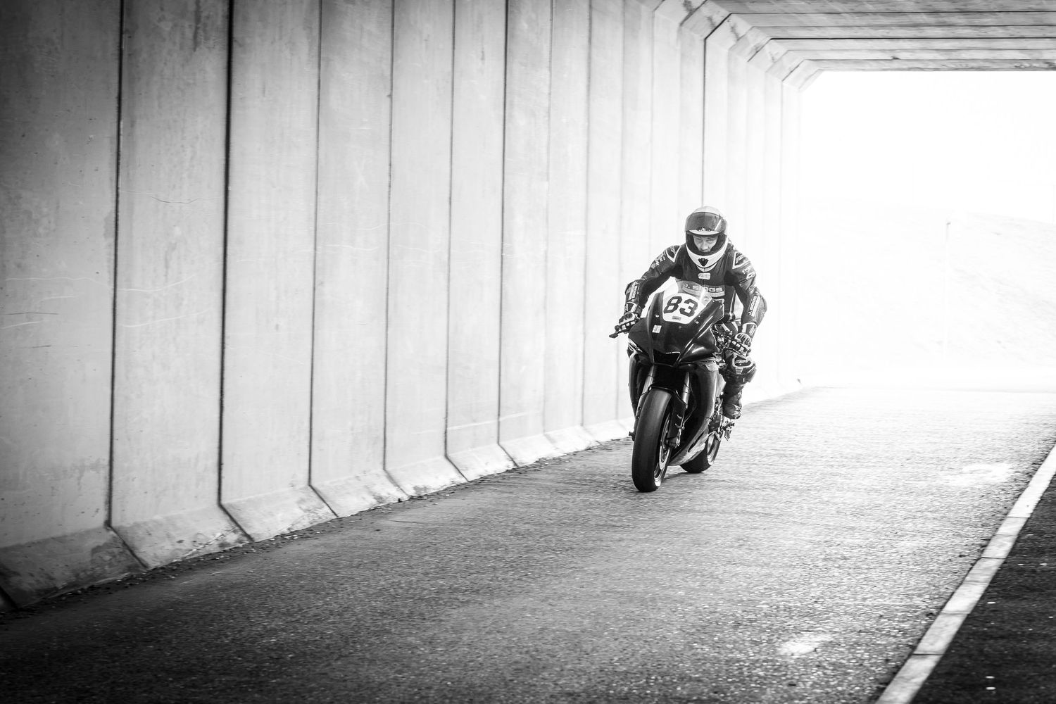 Black and white photo of a motorcycle racer numbered 93 speeding through a tunnel on a race track.