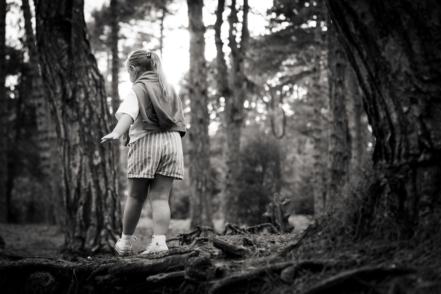 Black and white photo of a young girl standing among tree roots in a misty forest.