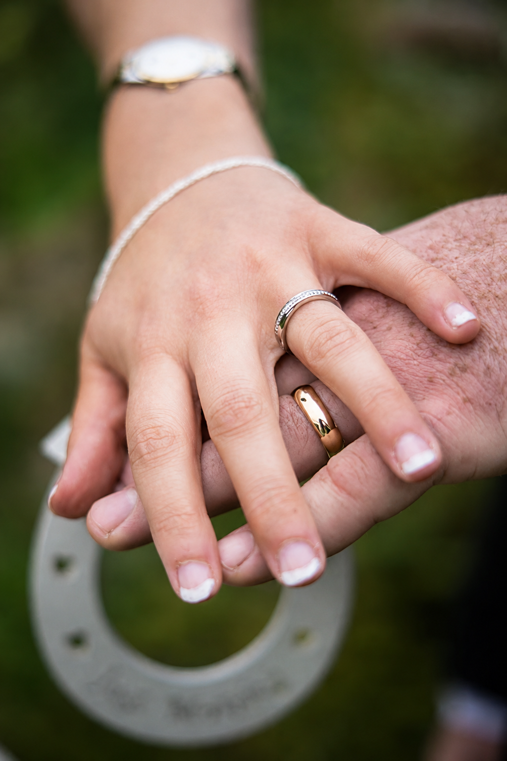 Close-up of a bride's hand with a silver ring resting on a groom's hand wearing a gold wedding band, with a silver horseshoe below.