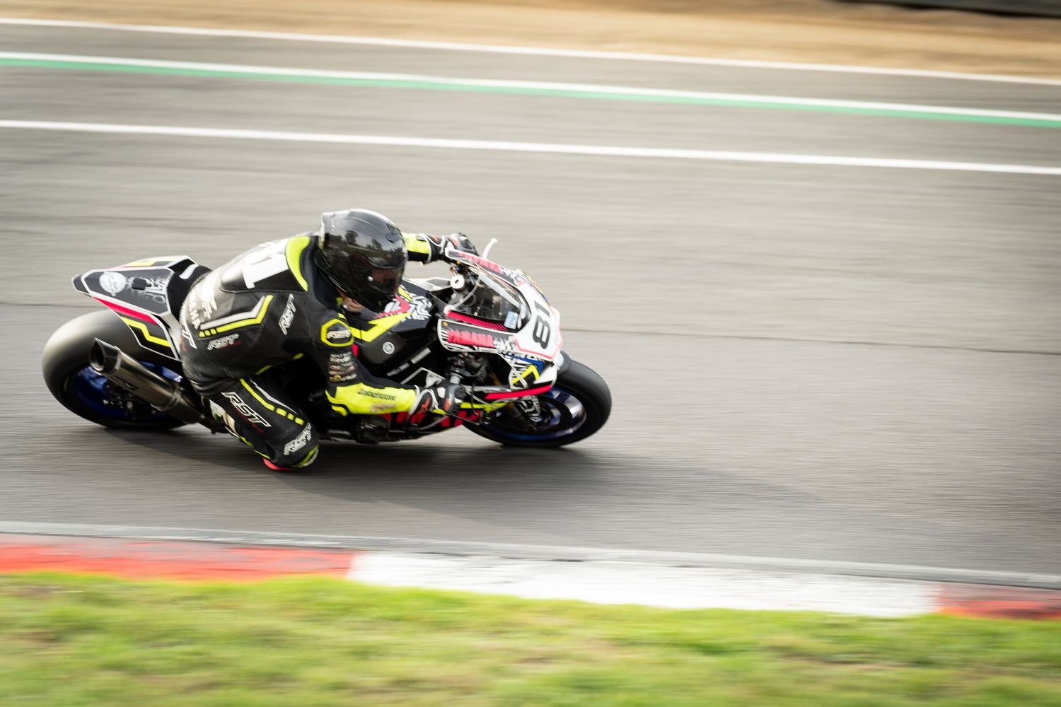 A motorcycle racer leans into a turn at high speed on a racing circuit, wearing black and yellow gear.