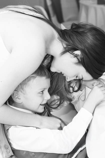 Black and white photo of a smiling young boy in a vest and white shirt embracing a dark-haired woman who leans down to him affectionately.