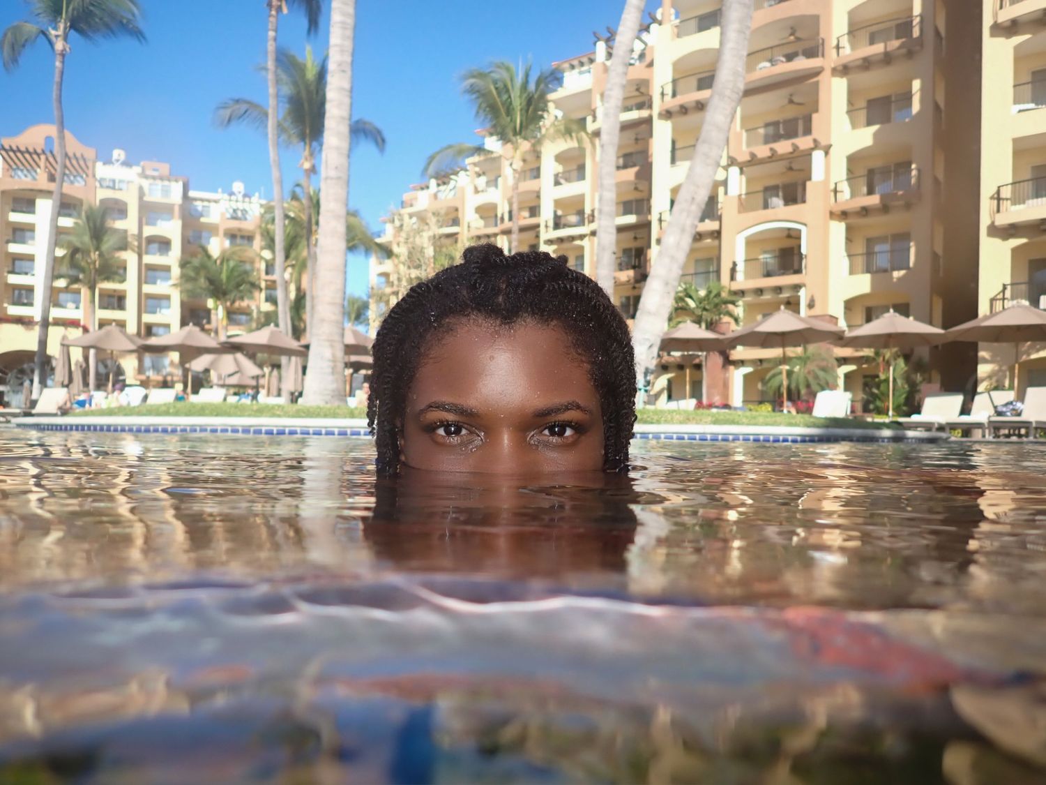 A woman in a hotel pool emerges from the water, with just her eyes and forehead visible above the water.